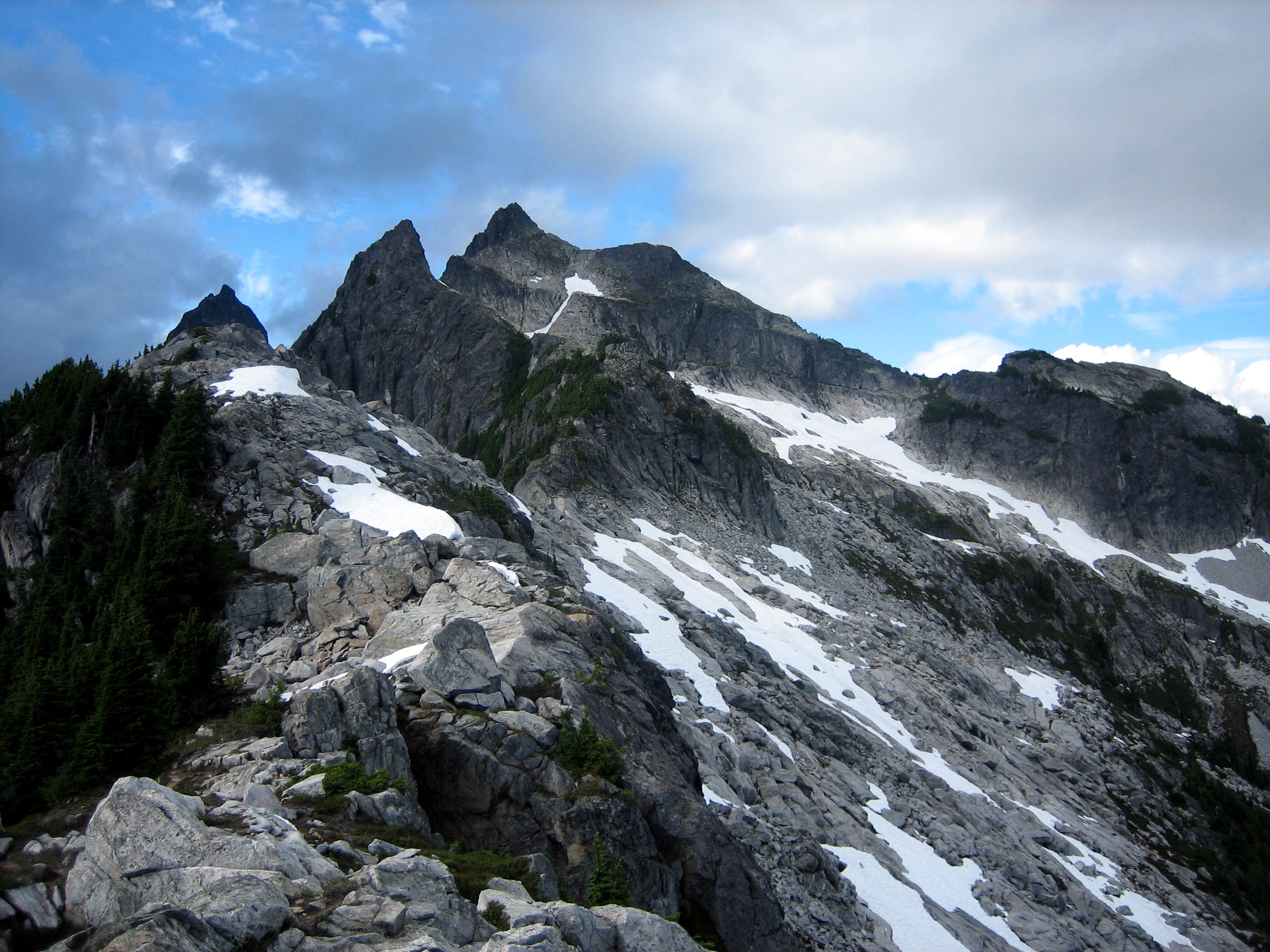 rock horn summit of Thornton Peak in the Lower Skagit Mountains with rock slopes, linguring snow patches, and patchy green heather in North Cascades National Park 