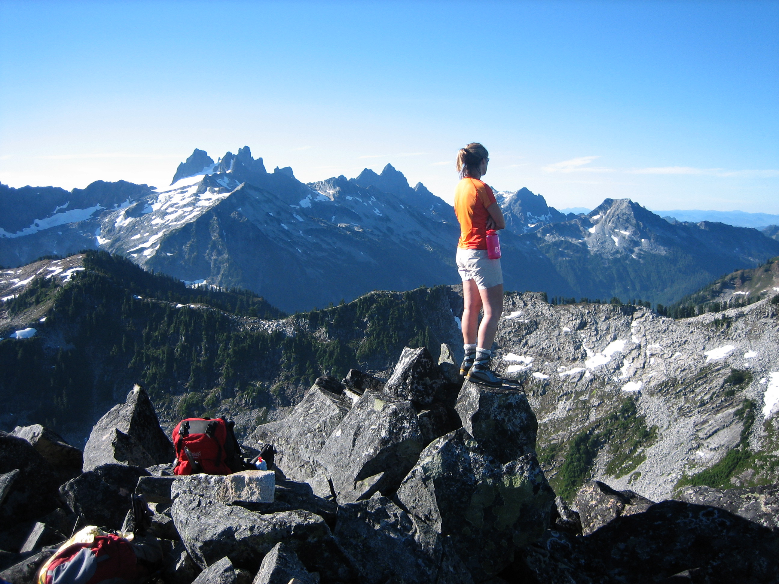 hiker on the rocky summit of Tourmaline Peak with the Snoqualmie Mountains in the background