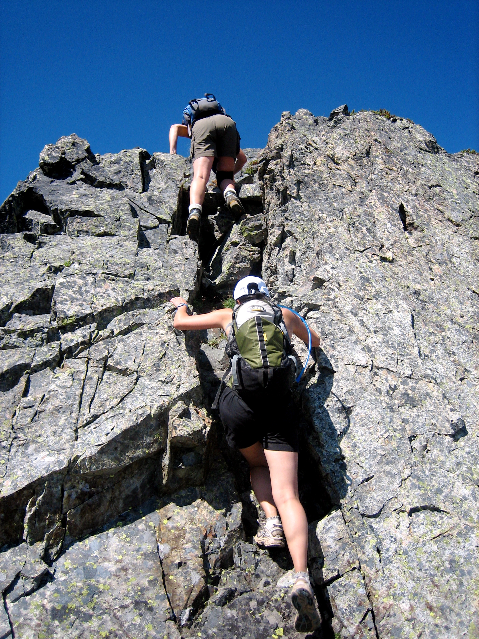 mountain climbers scrambling rocky slot on steep summit horn of Hibox Peak in the Snoqualmie Mountains