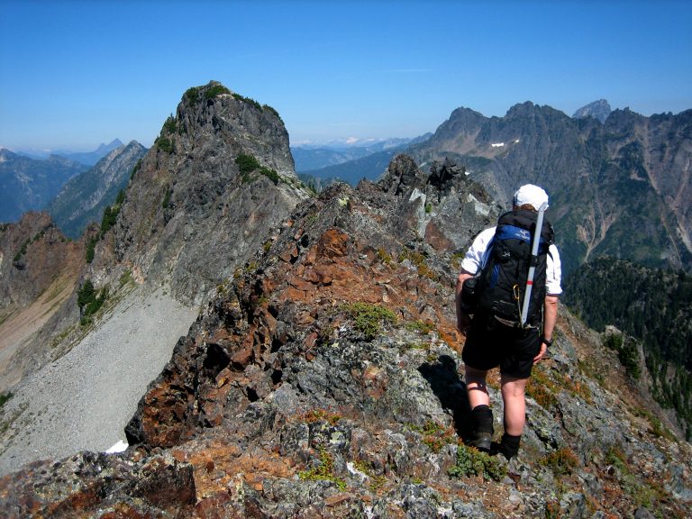A mountain climber traverses the crest of a rocky ridge toward Silvertip Peak