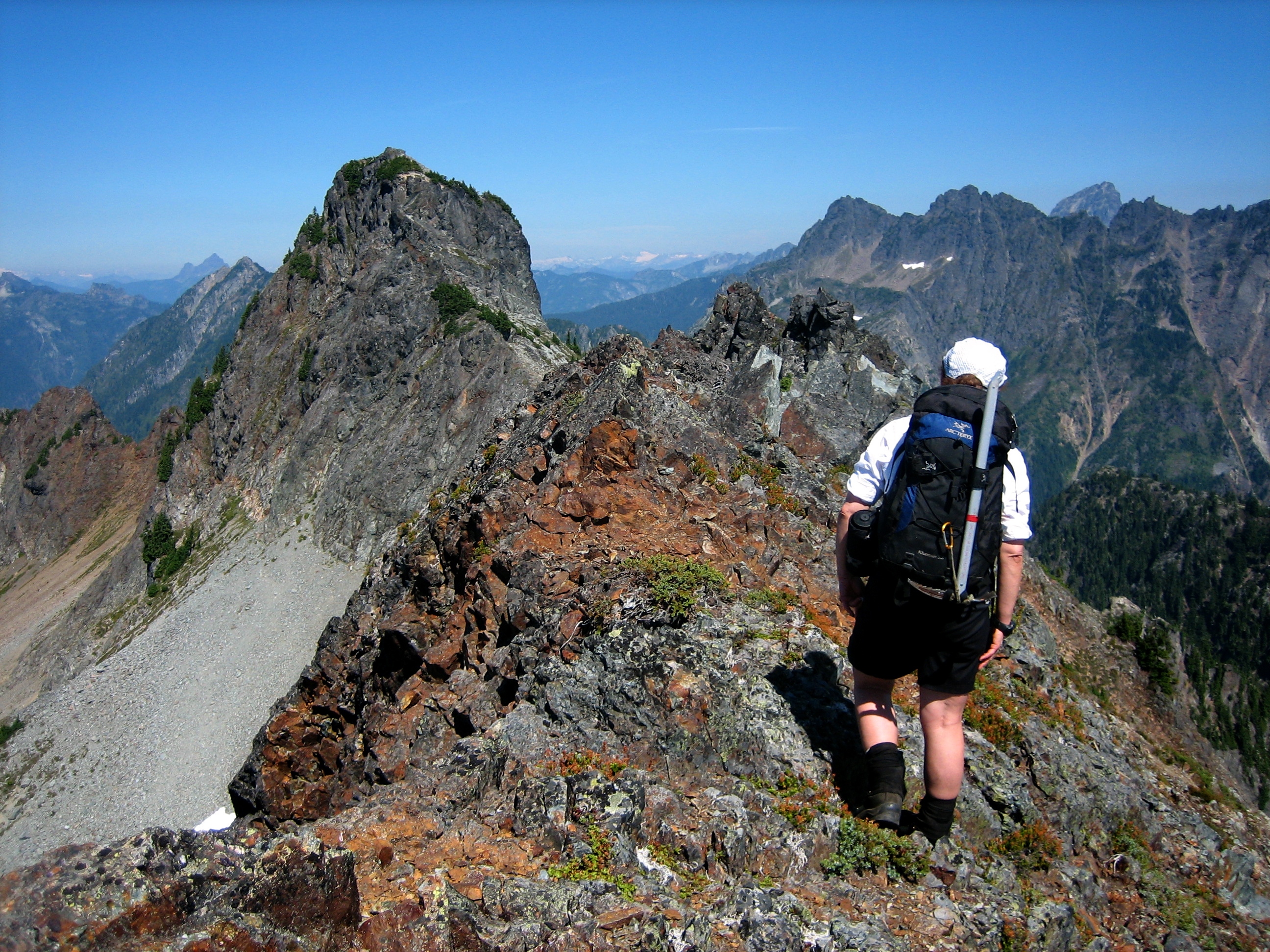 A mountain climber traverses the crest of a rocky ridge toward Silvertip Peak