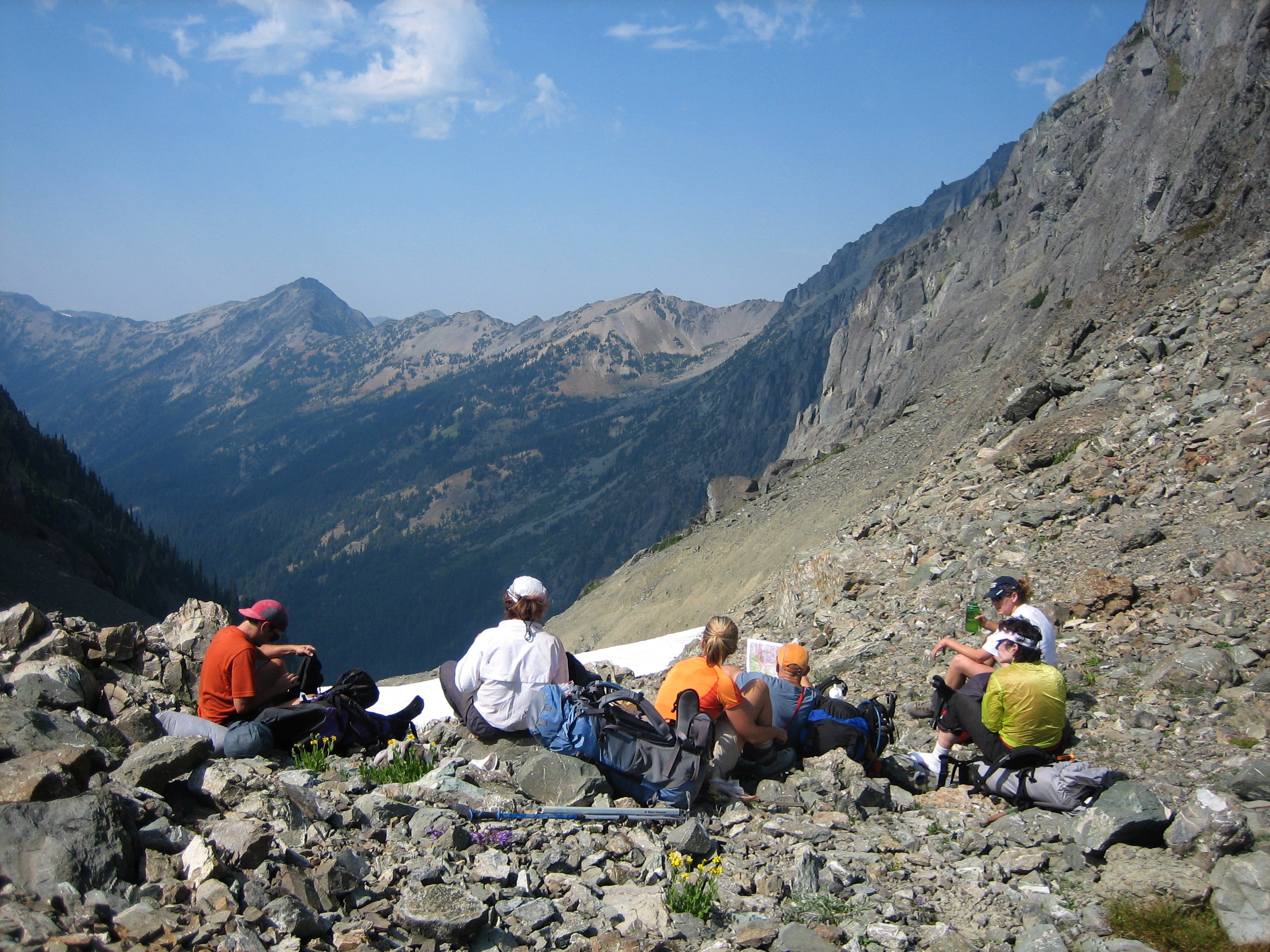 backpackers taking a break on the rocky Gunsight Pass with snow patches looking into the Olympic Mountains