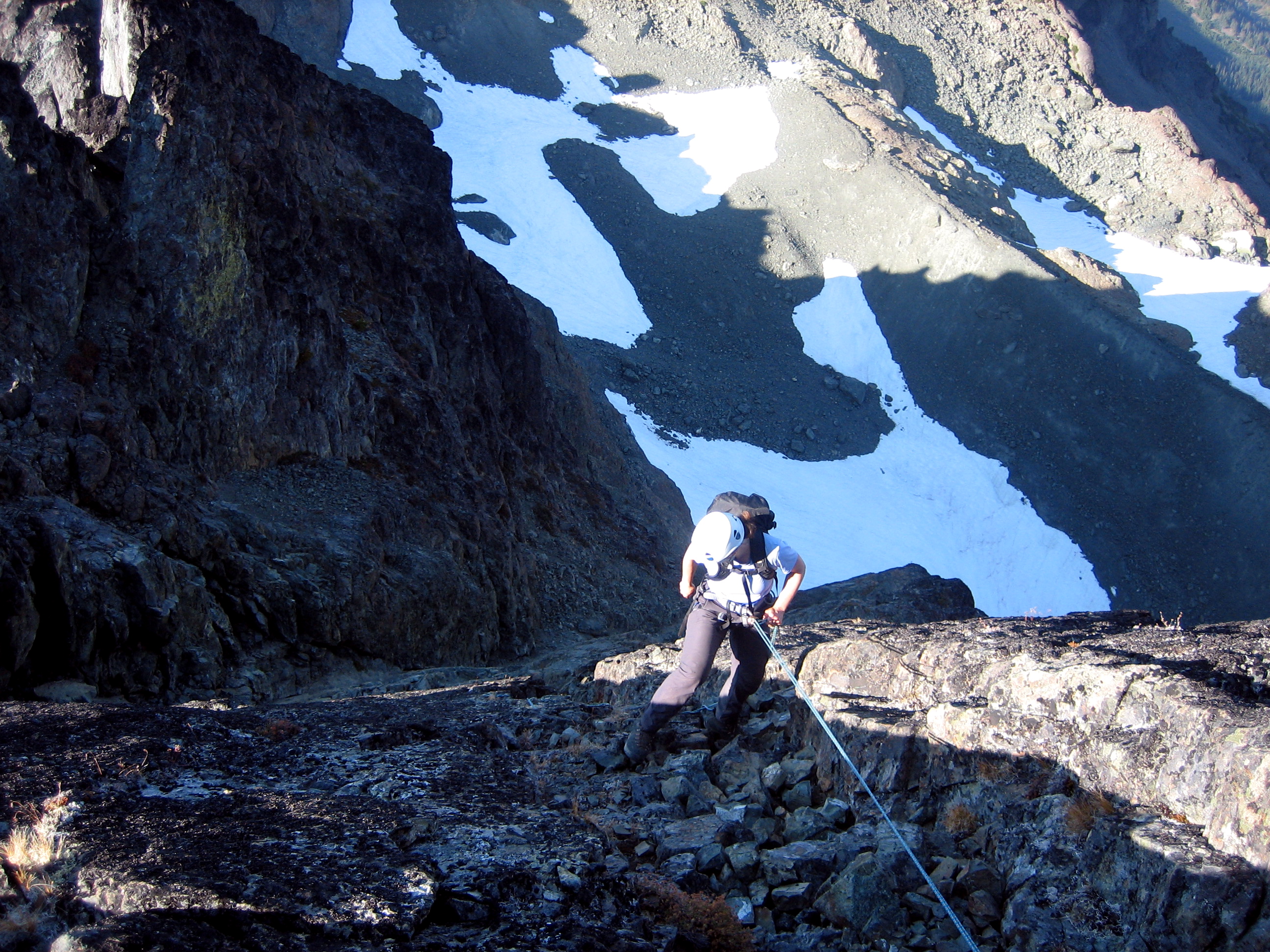 mountain climber rappelling off the rocky summit of Mt Clark with snow fields in the background 