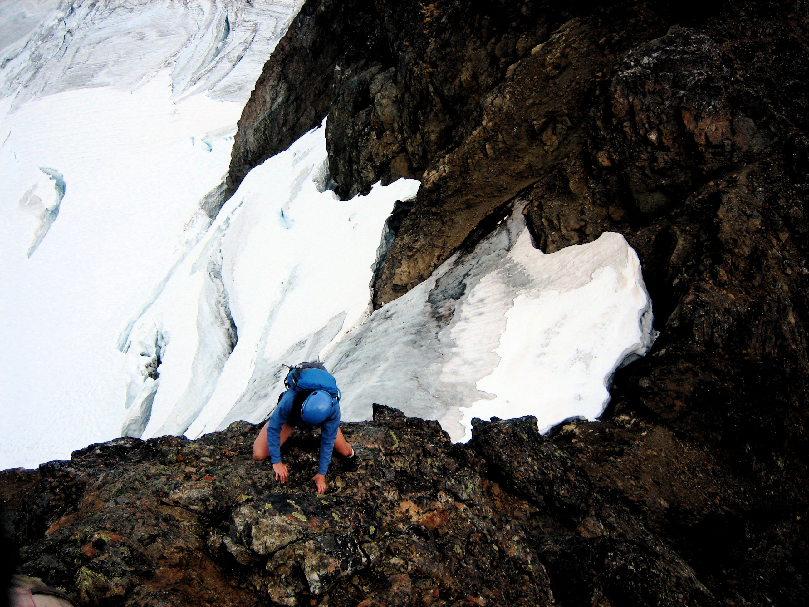 A rock climber scrambles a steep face on Tomyhoi Peak above a glacier in the Nooksack Mountains