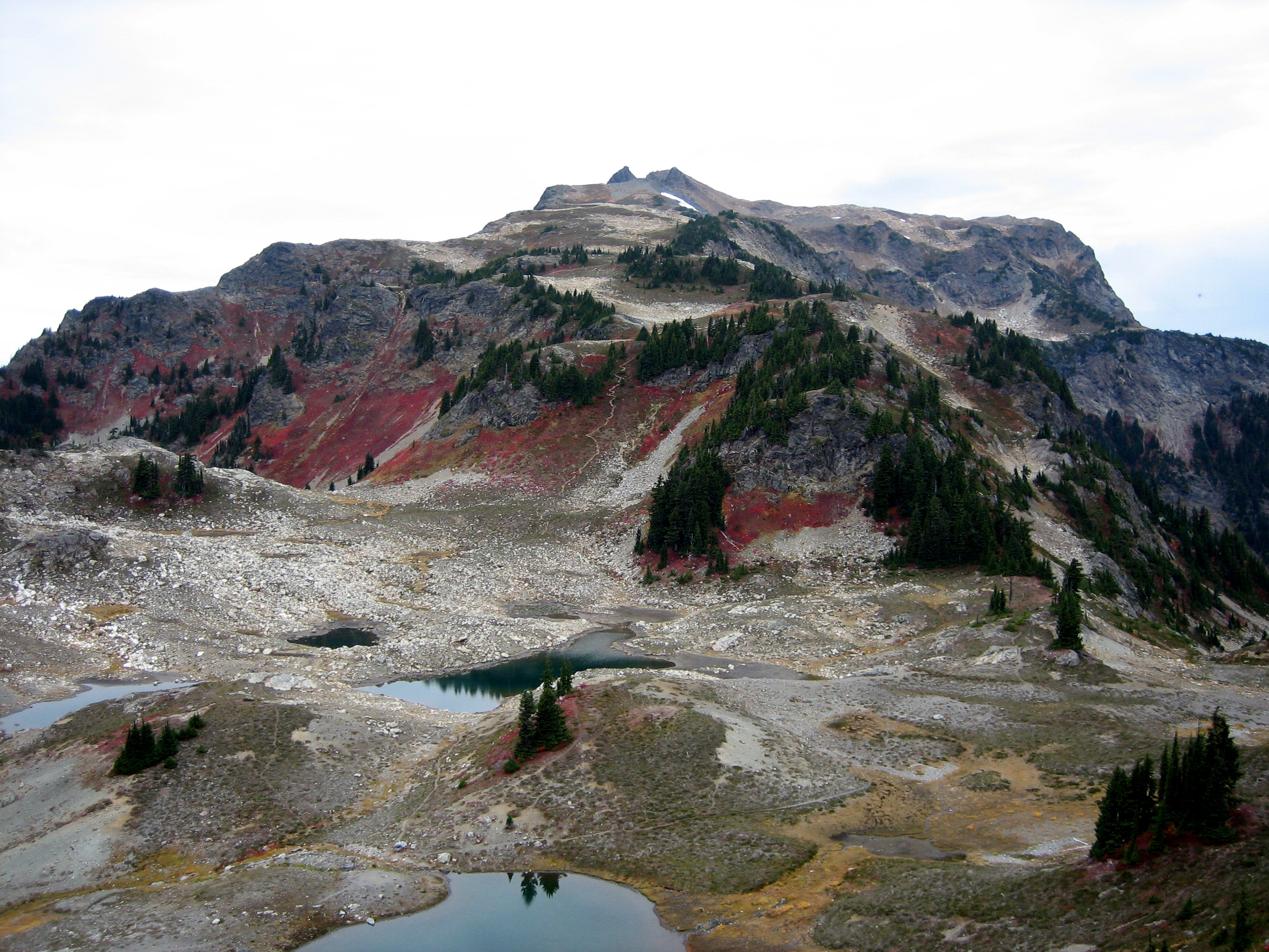 High summit horn on Tomyhoi Peak with Yellow Aster Lake in the foreground engulfed in fall colors in the Nooksack Mountains