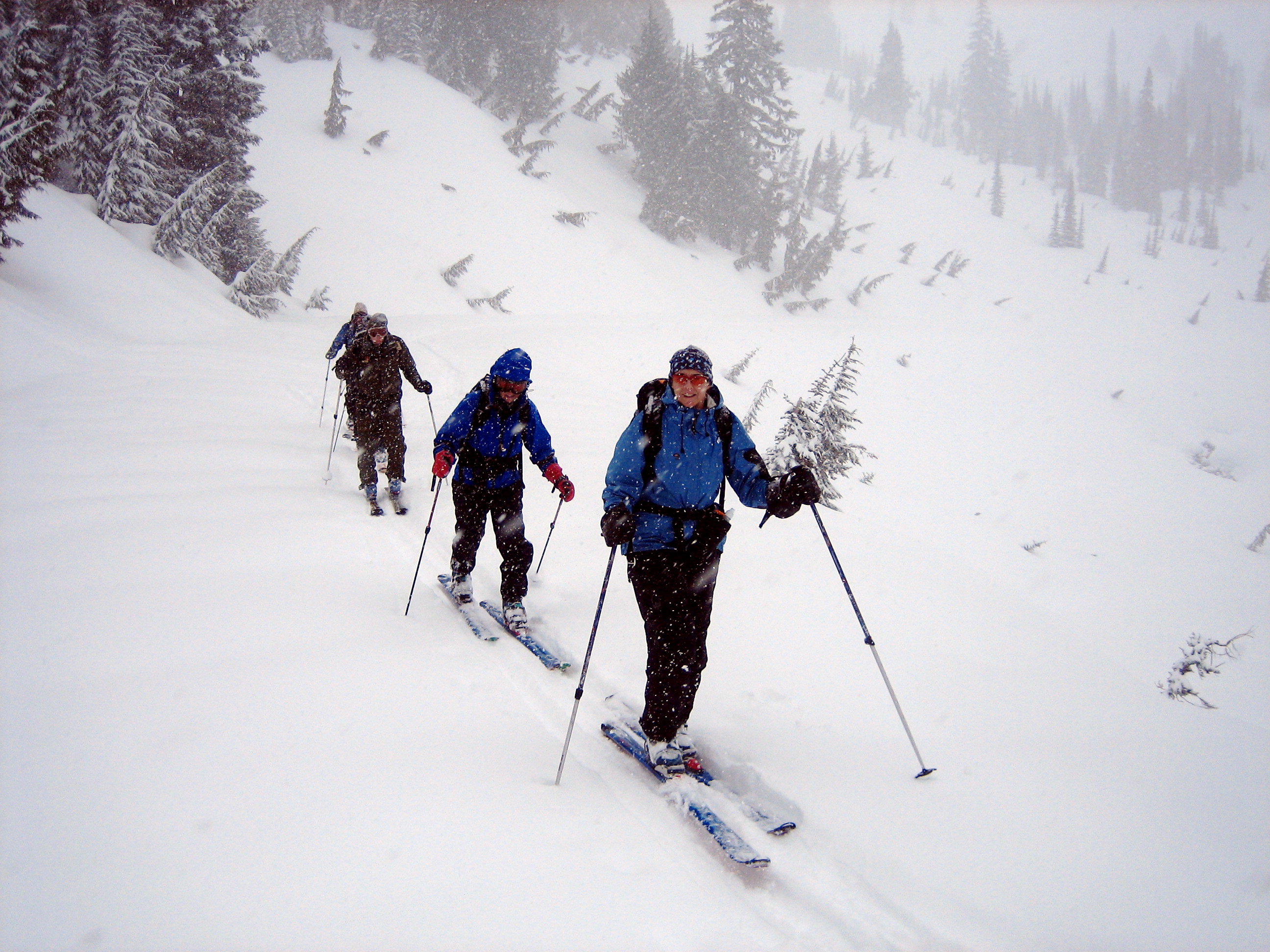 Three backcountry skiers glide up a snowy path toward Mazama Ridge in a blizzard