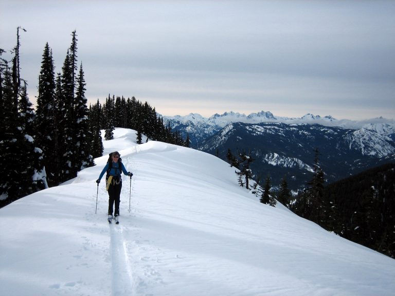 A backcountry skier glides along a flat ridge crest to Middle Jolly Knoll
