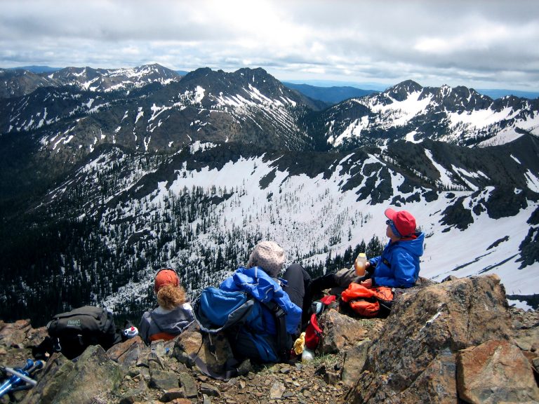 Three climbers relax on the summit of Longs Peak overlooking snowy mountains