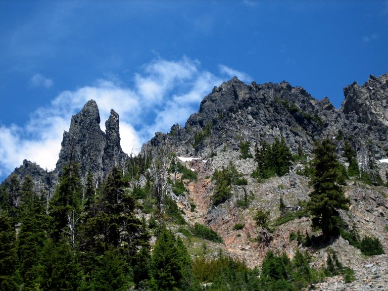 Looking up at rugged Middle Queen Mountain with rock horns against a blue sky