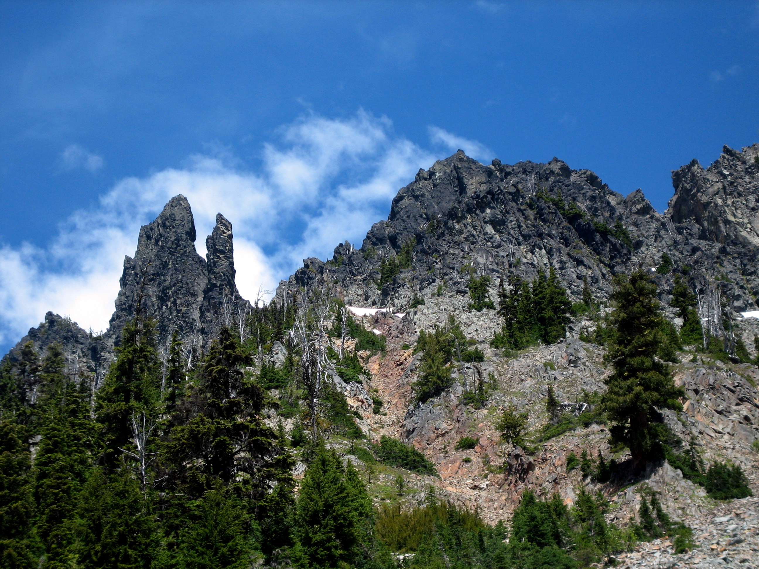 Looking up at rugged Middle Queen Mountain with rock horns against a blue sky