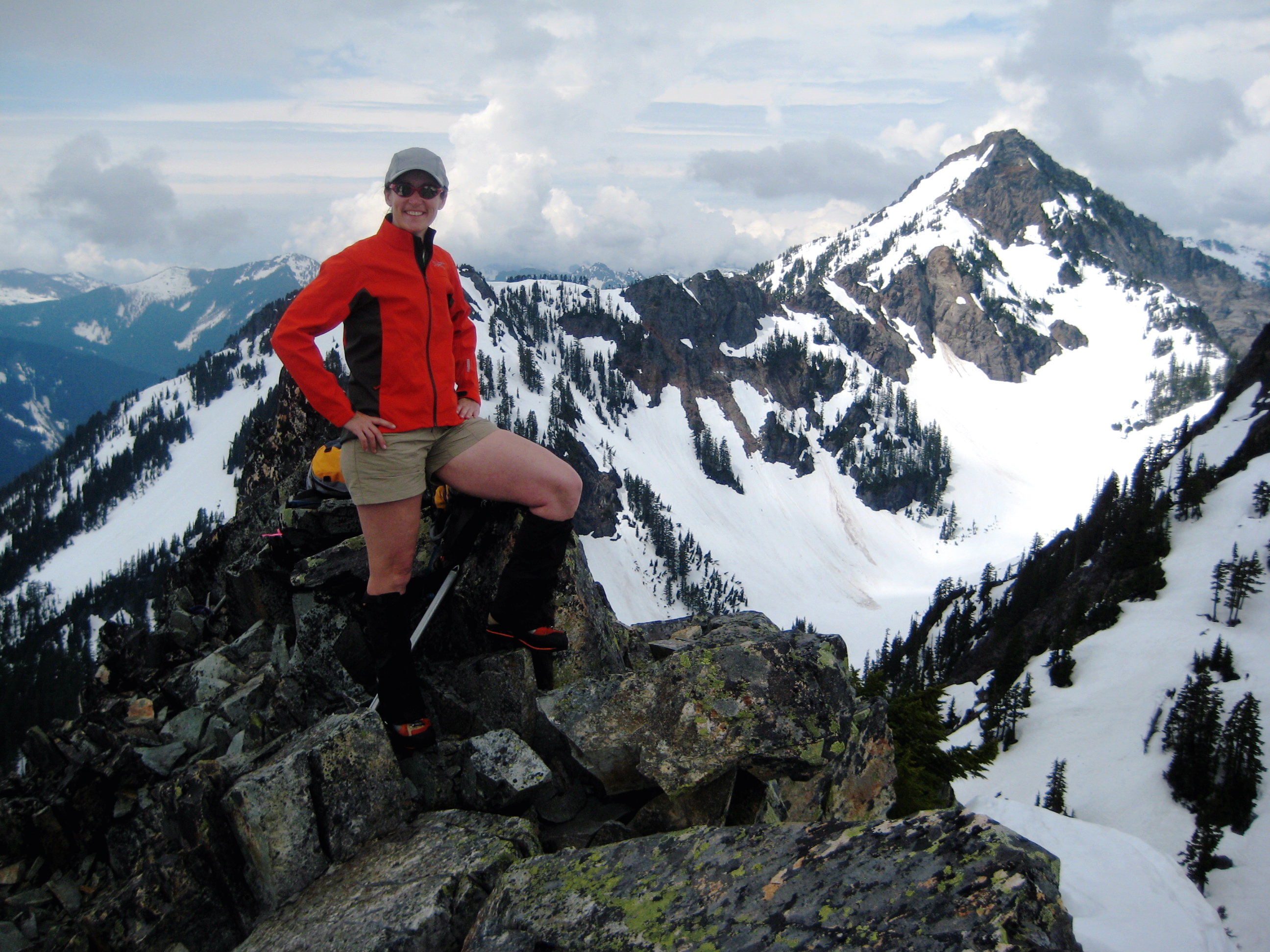 A woman in orange coat stands atop Bryant Peak in the Snoqualmie Mountains