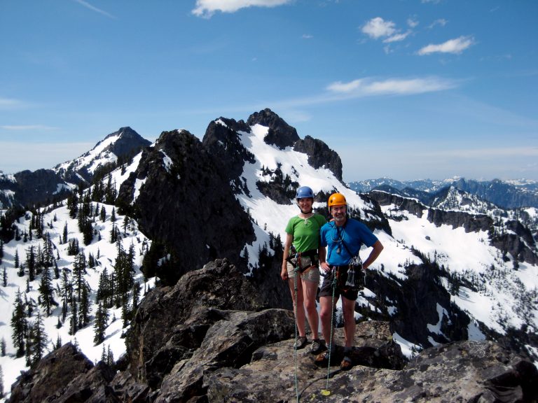 Two climbers stand on summit of The Snoqualmie Tooth surrounded by snowy peaks