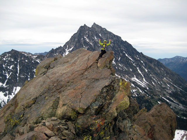 A mountain climber stradles a narrow summit horn on North Ingalls Peak