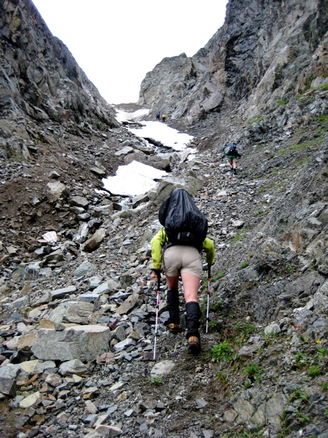 mountain climbers scramble loose rock gully leading to SIlent Lakes in North Cascades National Park with linguring snow patches and high rock walls