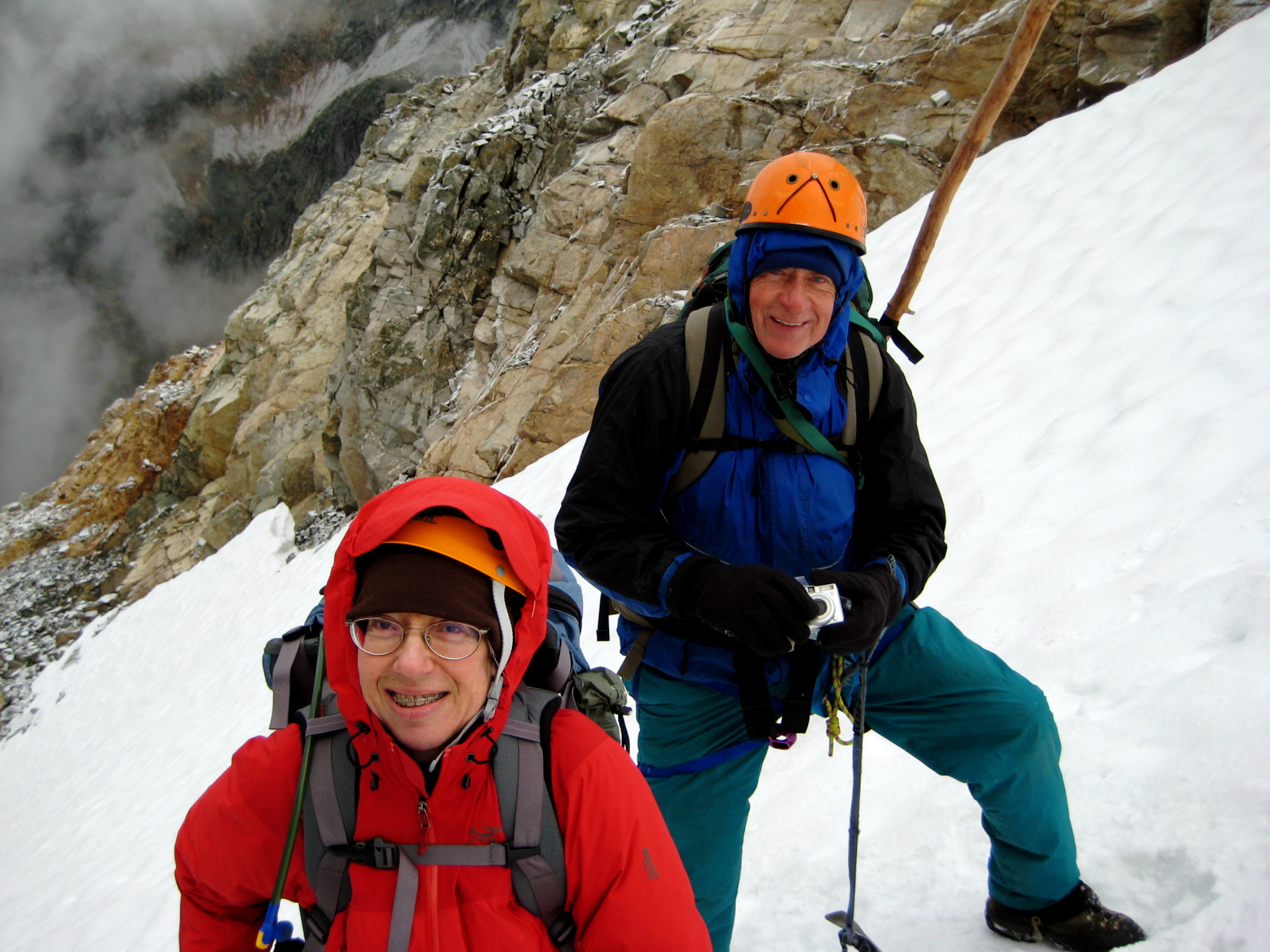 closeup of roped mountain climbers standing on steep snow slope with rock slabs in the background