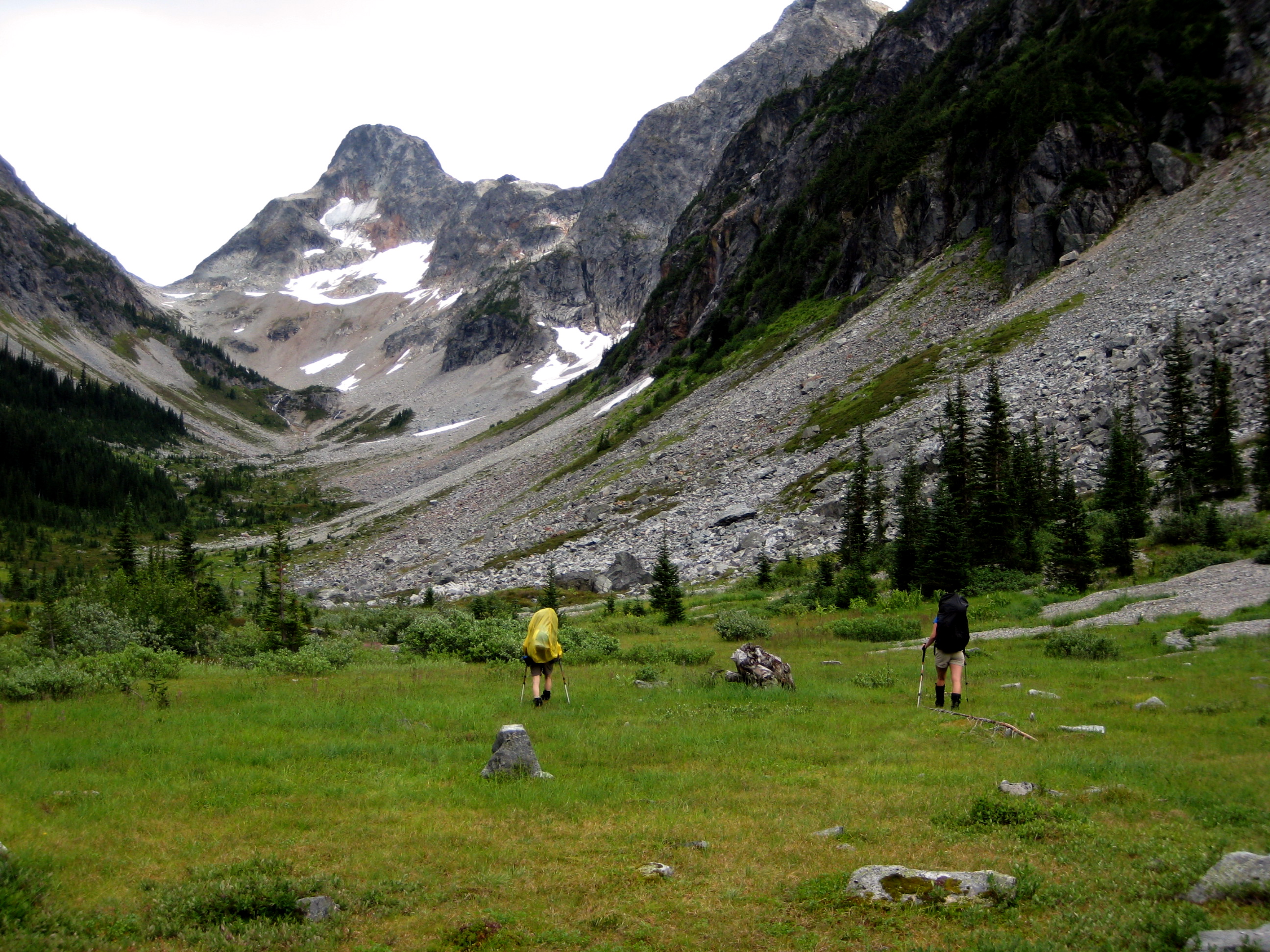 mountain climbers hiking up the green meadow of Fisher Creek Basin with Ragged Range mountains in the background 