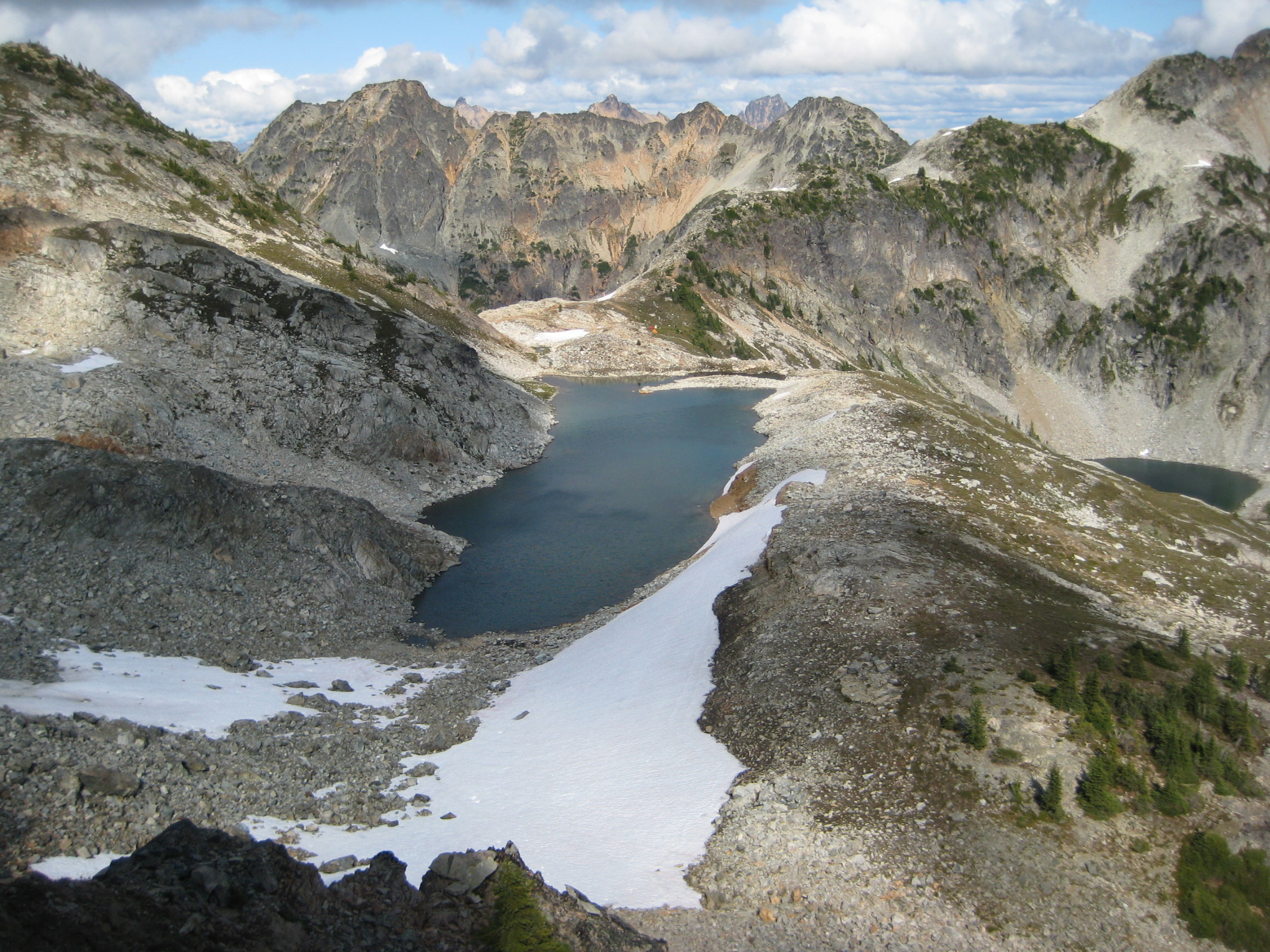 looking down on Silent Lakes in North Cascades National Park with scree fields and large snow patched with the Ragged Ridge mountain range in the background