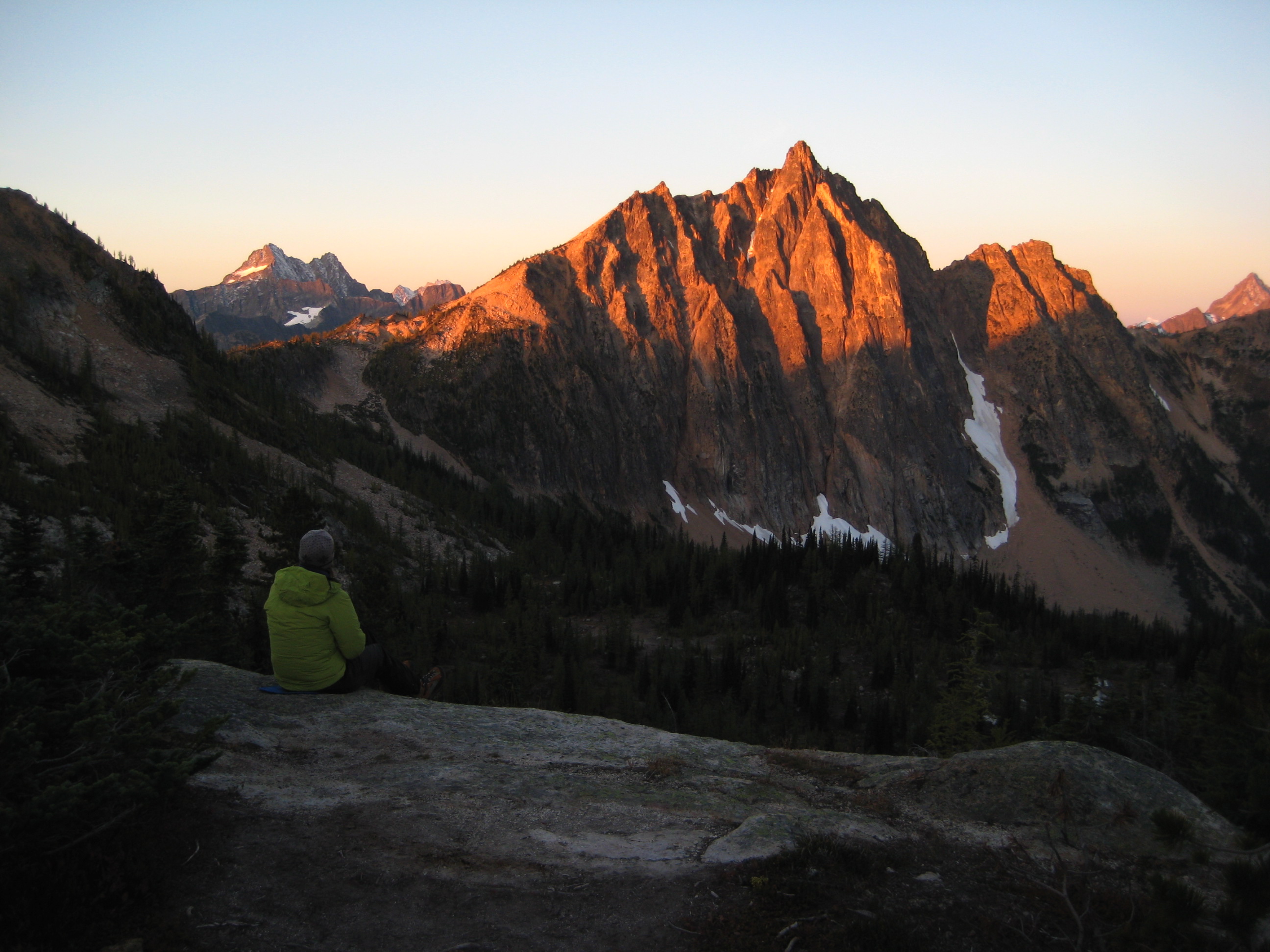Morning sunrise on Black Peak and Mt Hardy in the Upper Methow Mountains with a mountain climber sitting on a rock slab