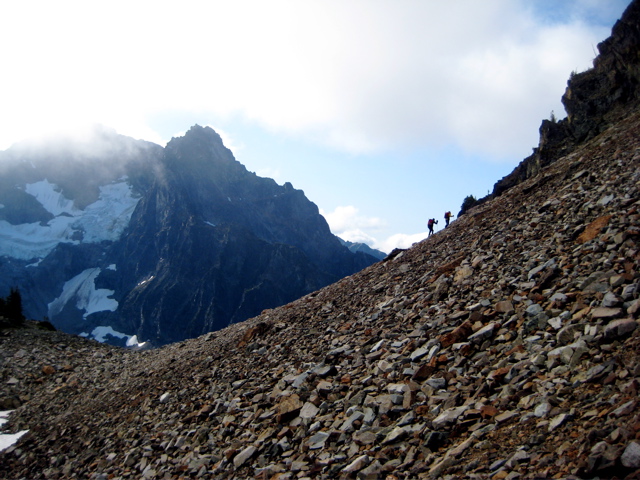 mountain climbers ascending large scree field with the Ragged RIdge mountain range of North Cascades National Park in the background