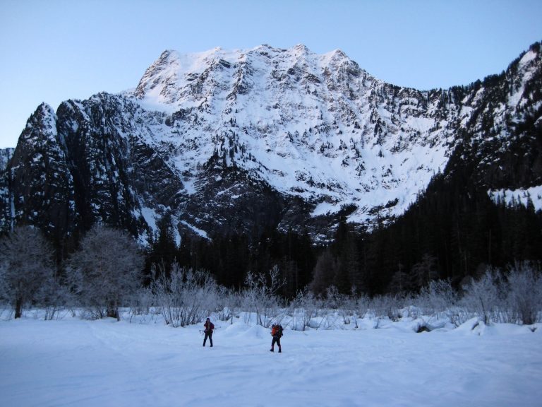 Hikers walk past the huge snowy north face of Big Four Mountain
