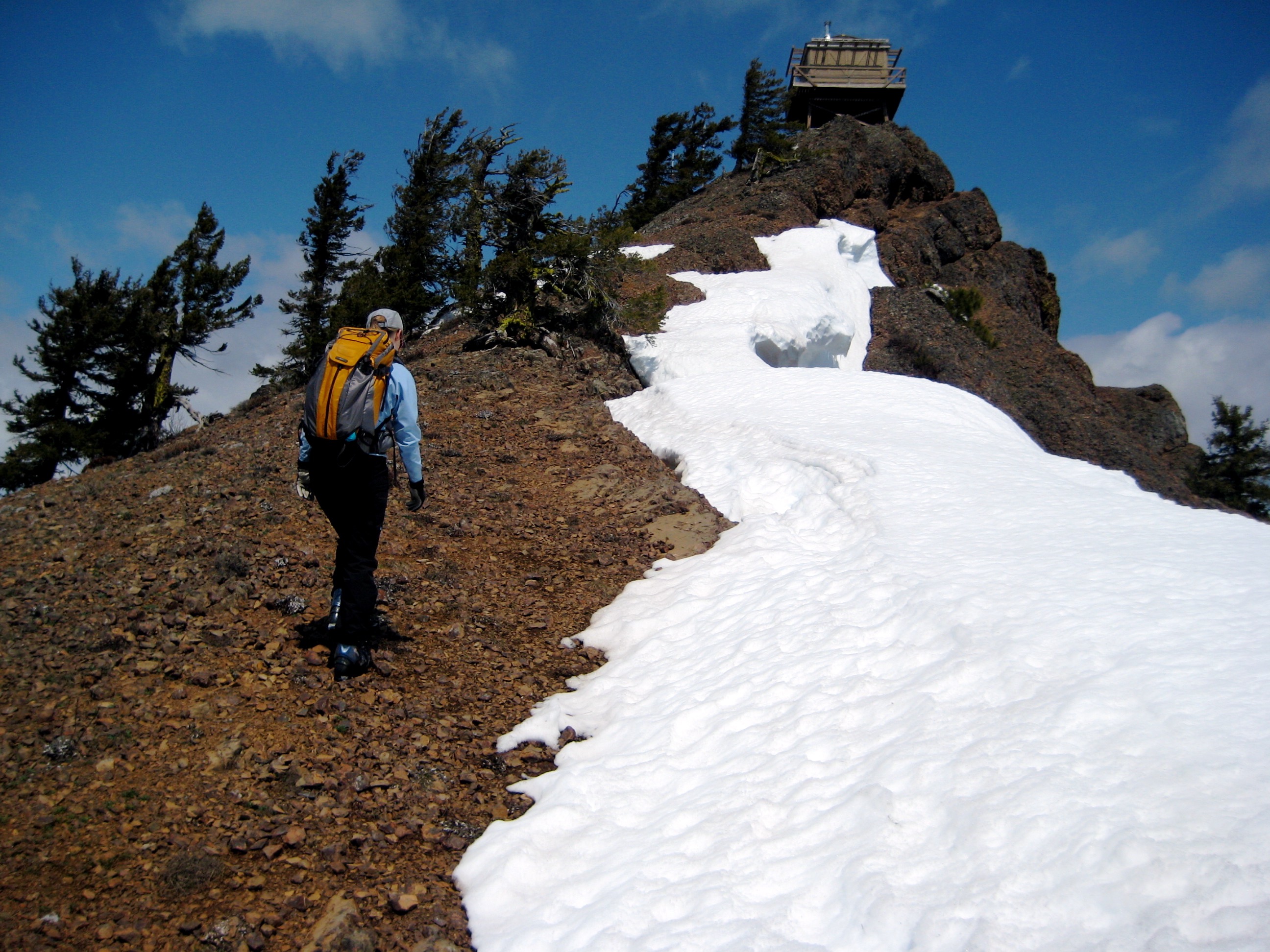 A hiker ascends red rock to the Red Top Mountain lookout cabin