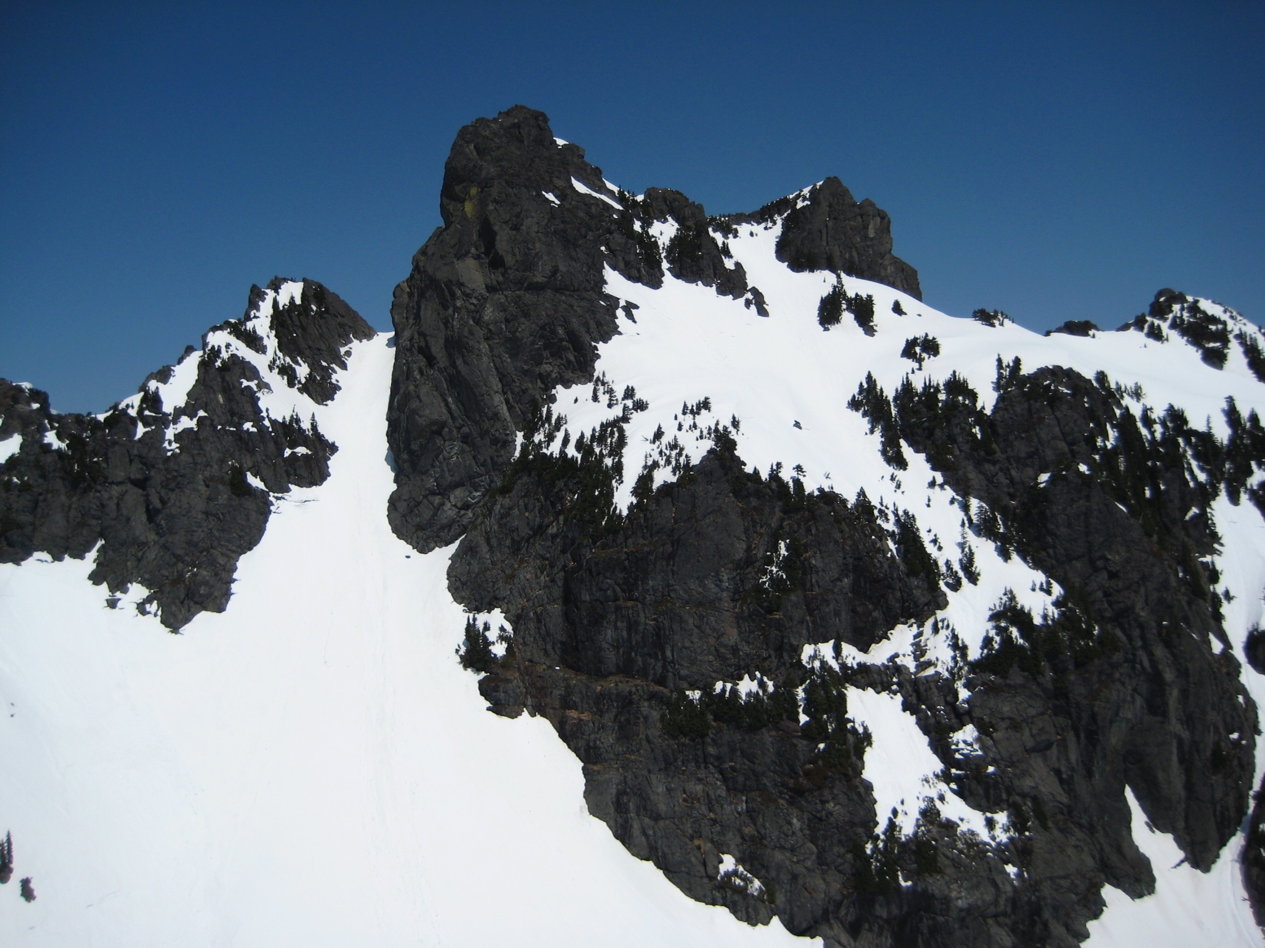 The twin rocky summits of Gunn Peak rise above a snow slope in the Skykomish Mountains