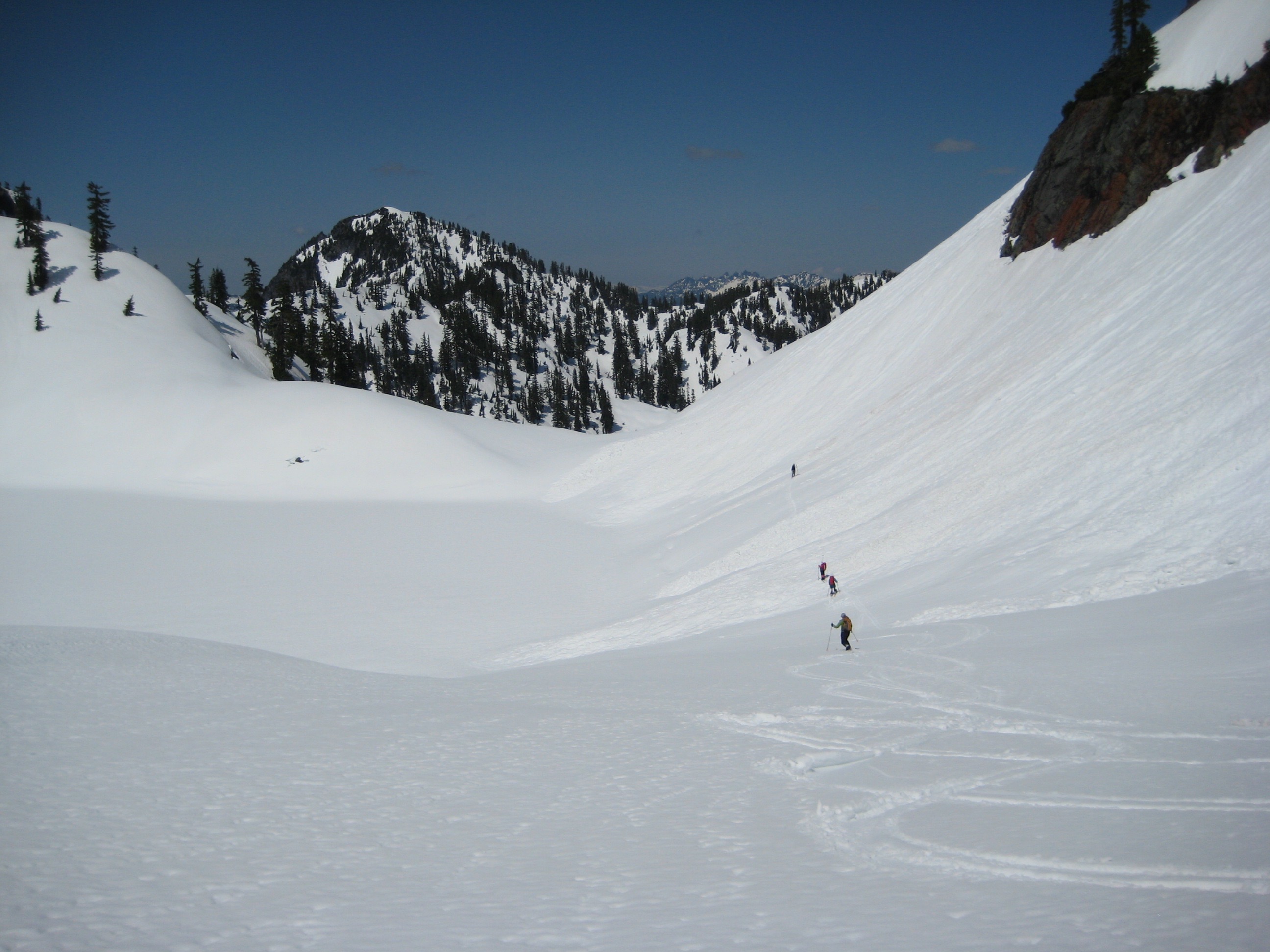 Backcountry skiers traverse a broad snow basin above Chair Peak Lake during the Chair Peak Ski Circumnavigation in the Snoqualmie Mountains
