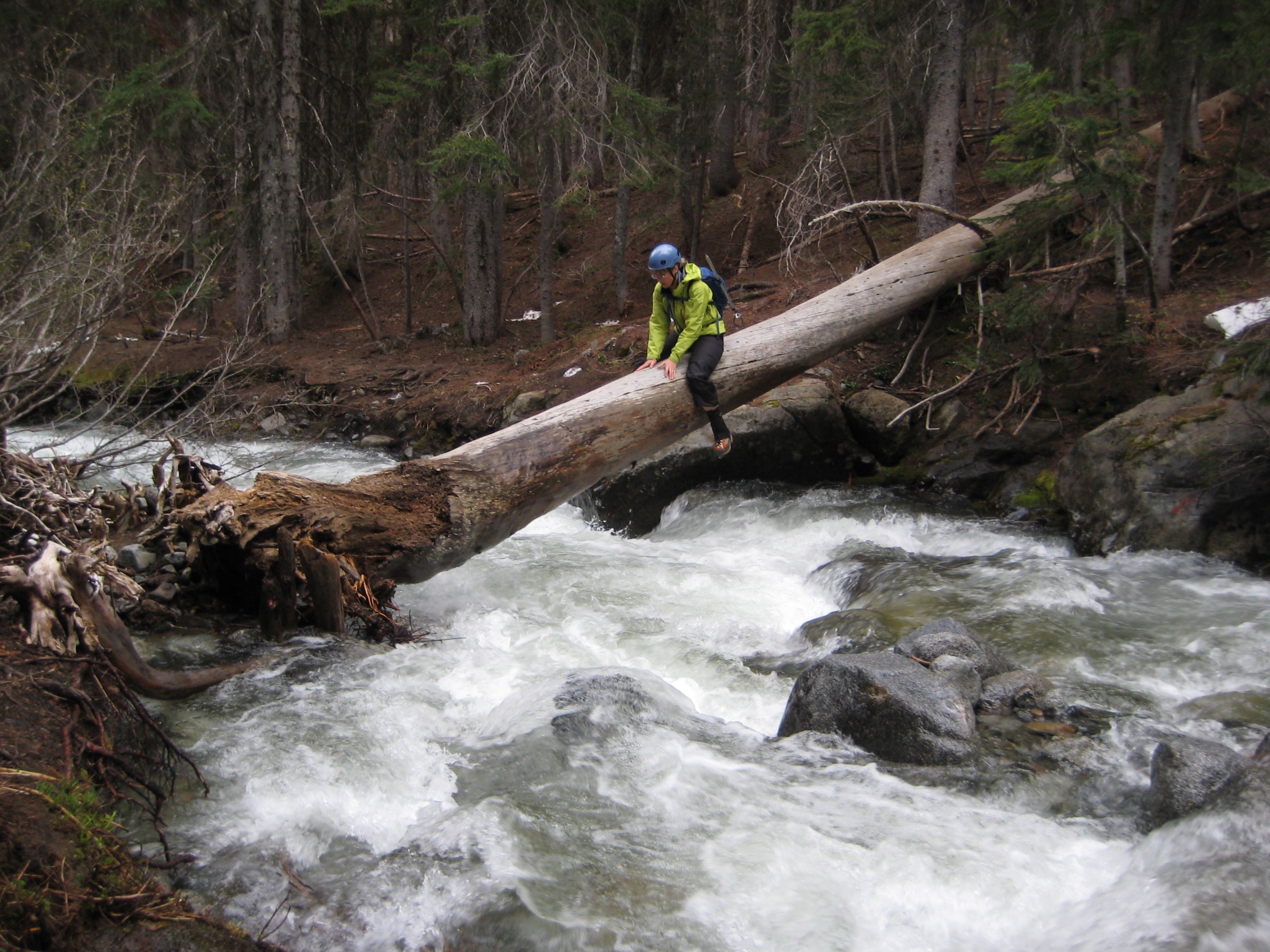 mountain climber sliding on a log across the ragging Icicle Creek in the Icicle Mountains