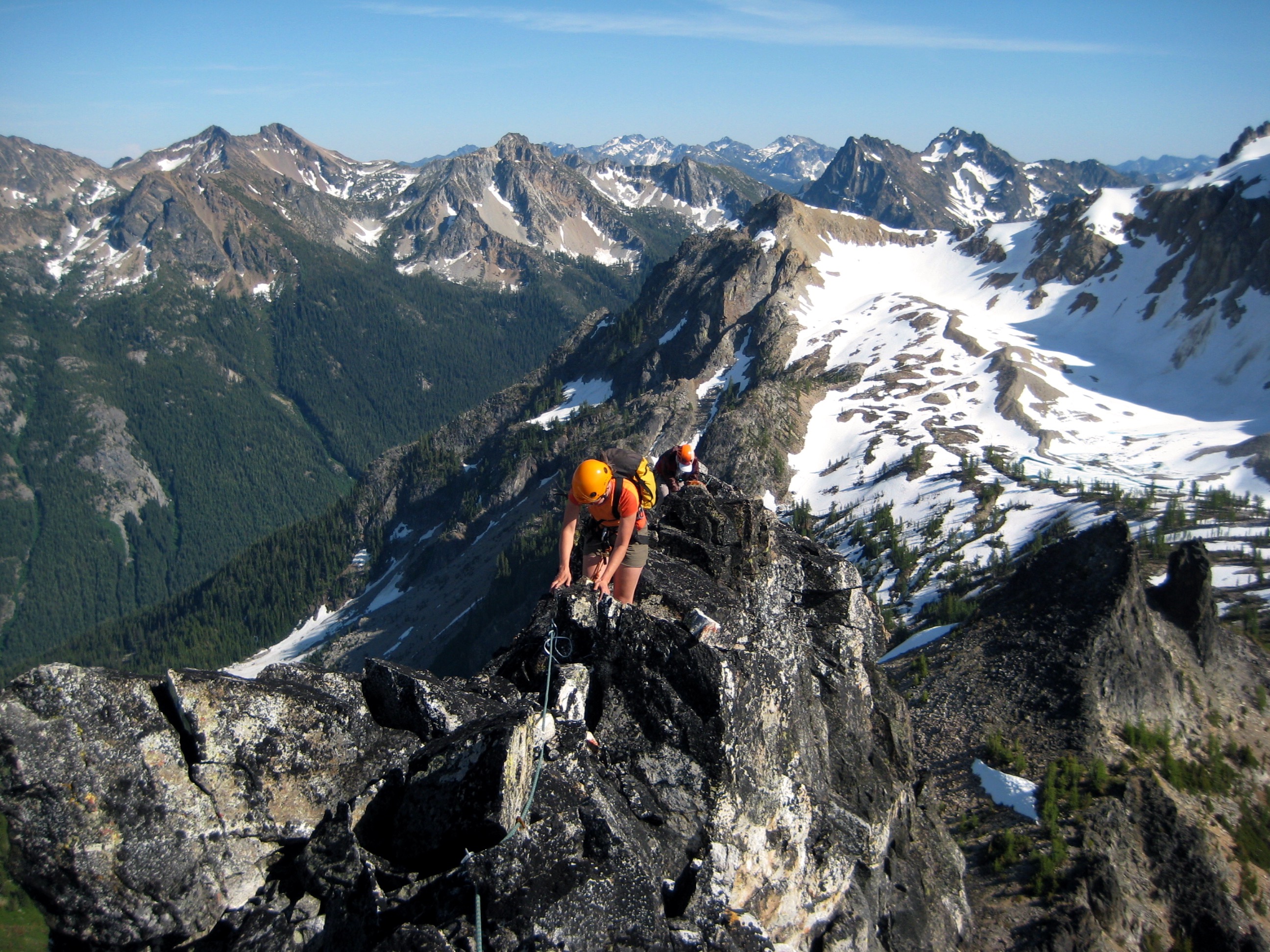 roped mountain climbers scrambling the very narrow ridge of White Goat Peak with the Stehekin Mountains in the background