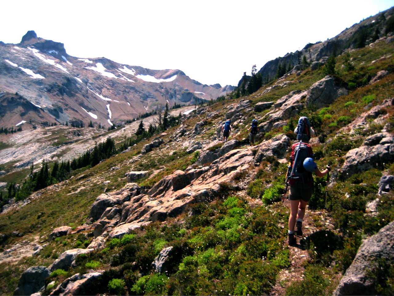 mountain climbers traversing heather and rock slabs on steep slope with The Citadel in the Alpine Lakes Wilderness
