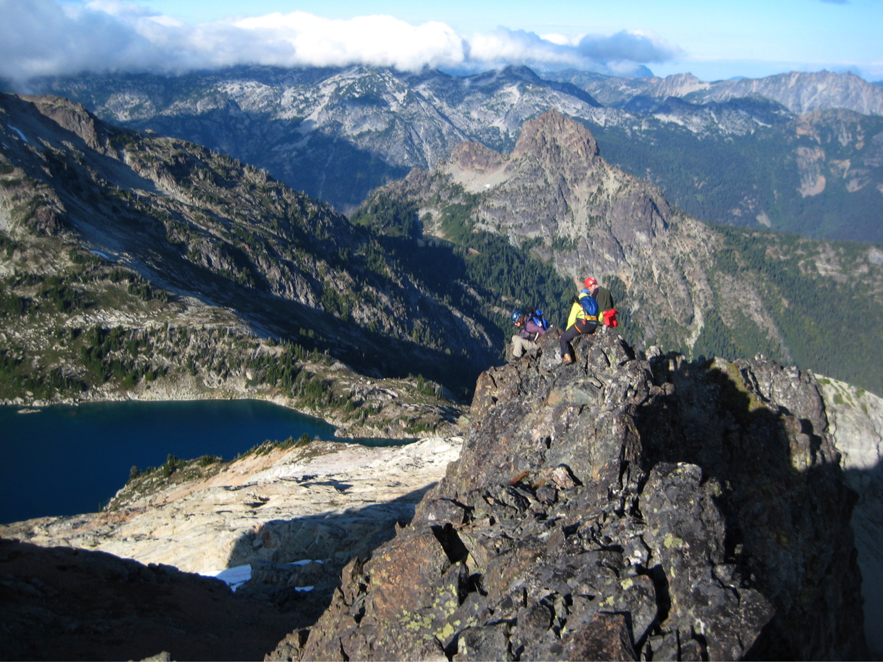 mountain climbers setting up a rappel station on the losse, rocky ridge of The Citadel with the Alpine Lakes Wilderness in the distance