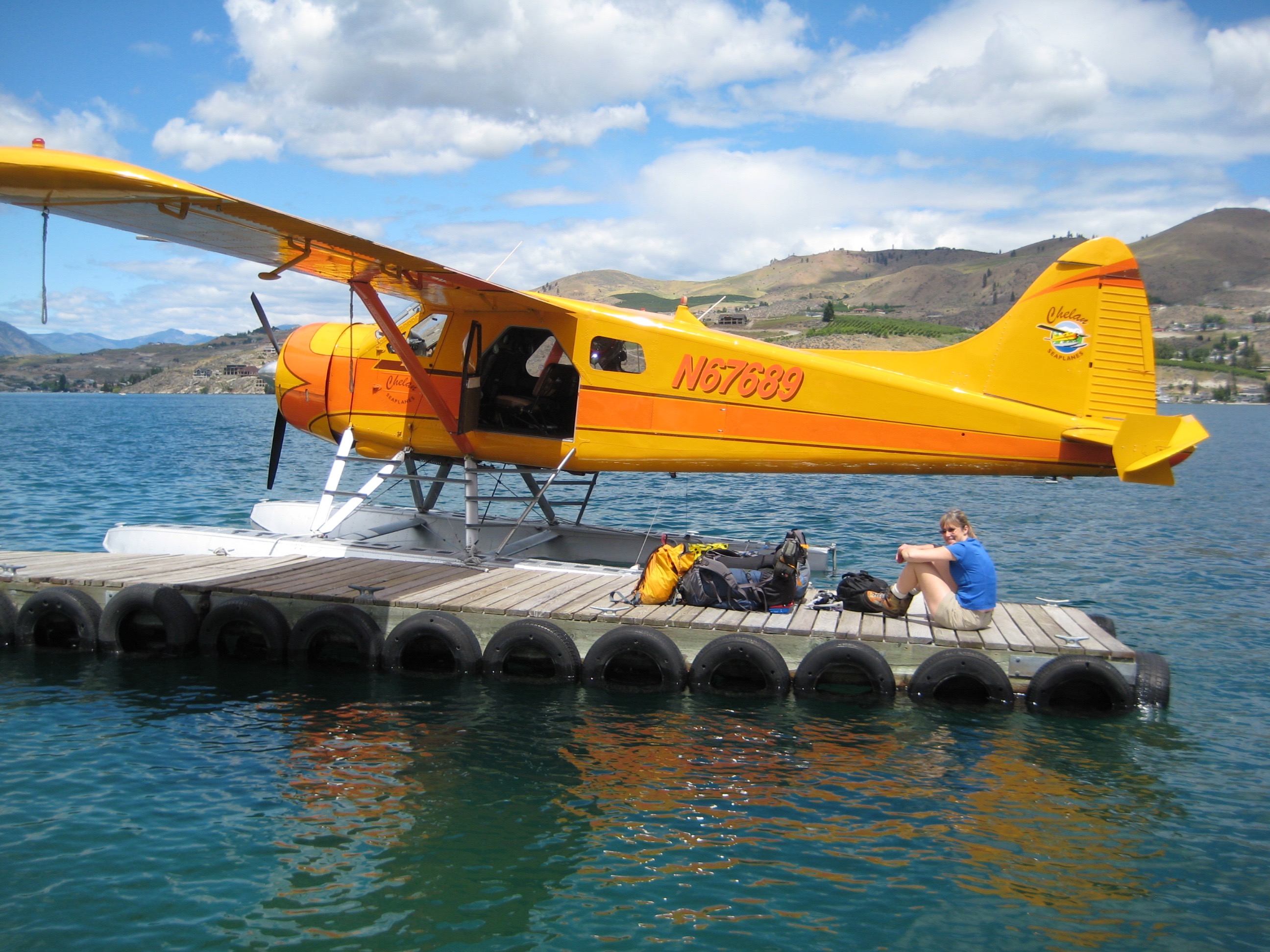 mountain climber with climbing packs sits on a wood dock on Lake Chelan with a yellow sea plane 