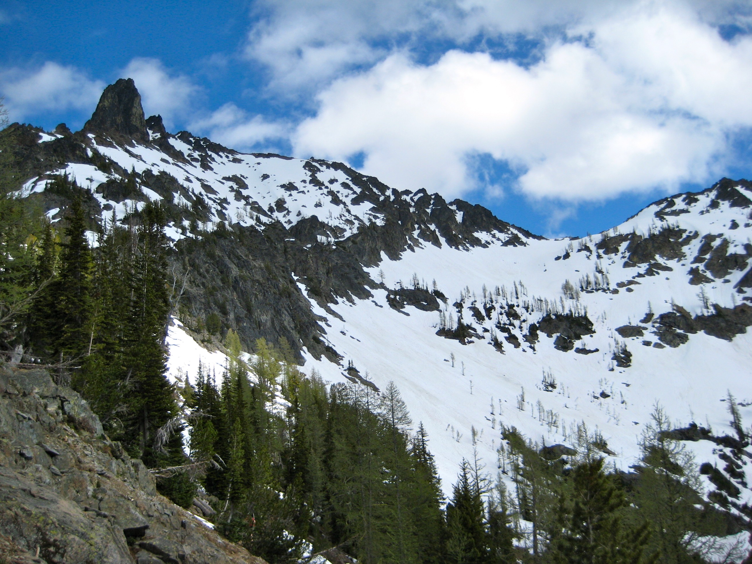 Main Riddle Peak summit horn jets into the blue sky with lower snow fields as seen from Tenmile Pass in the Stehekin Mountains