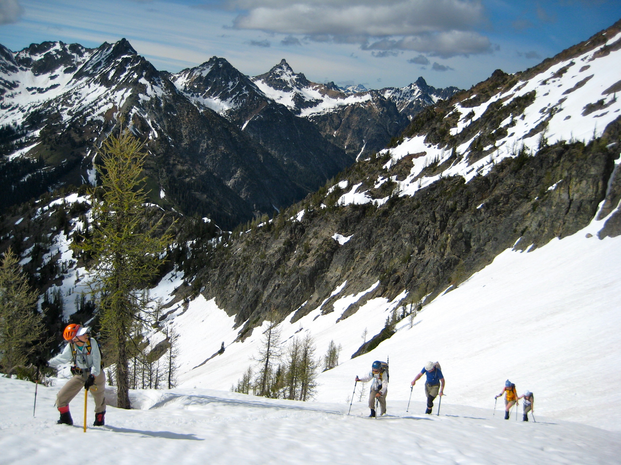 mountain climbers boot up snow field on the way to Main RIddle Peak with the mountains of the Glacier Peak Wilderness in the background