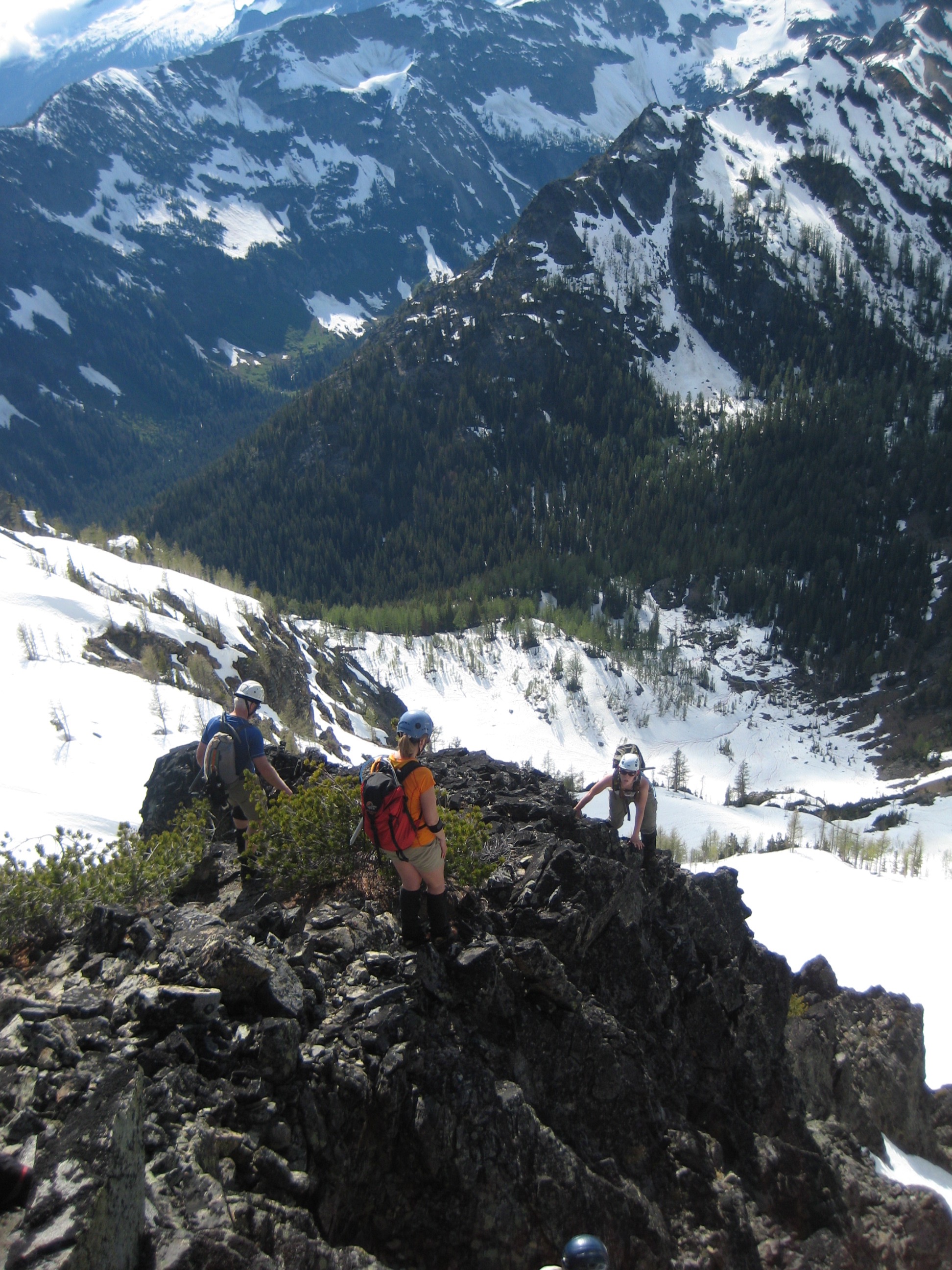 looking down on mountain climbers scrambling the rocky shoulder of Riddle Peak in Glacier Peak Wilderness with a snow filed valley in gthe background