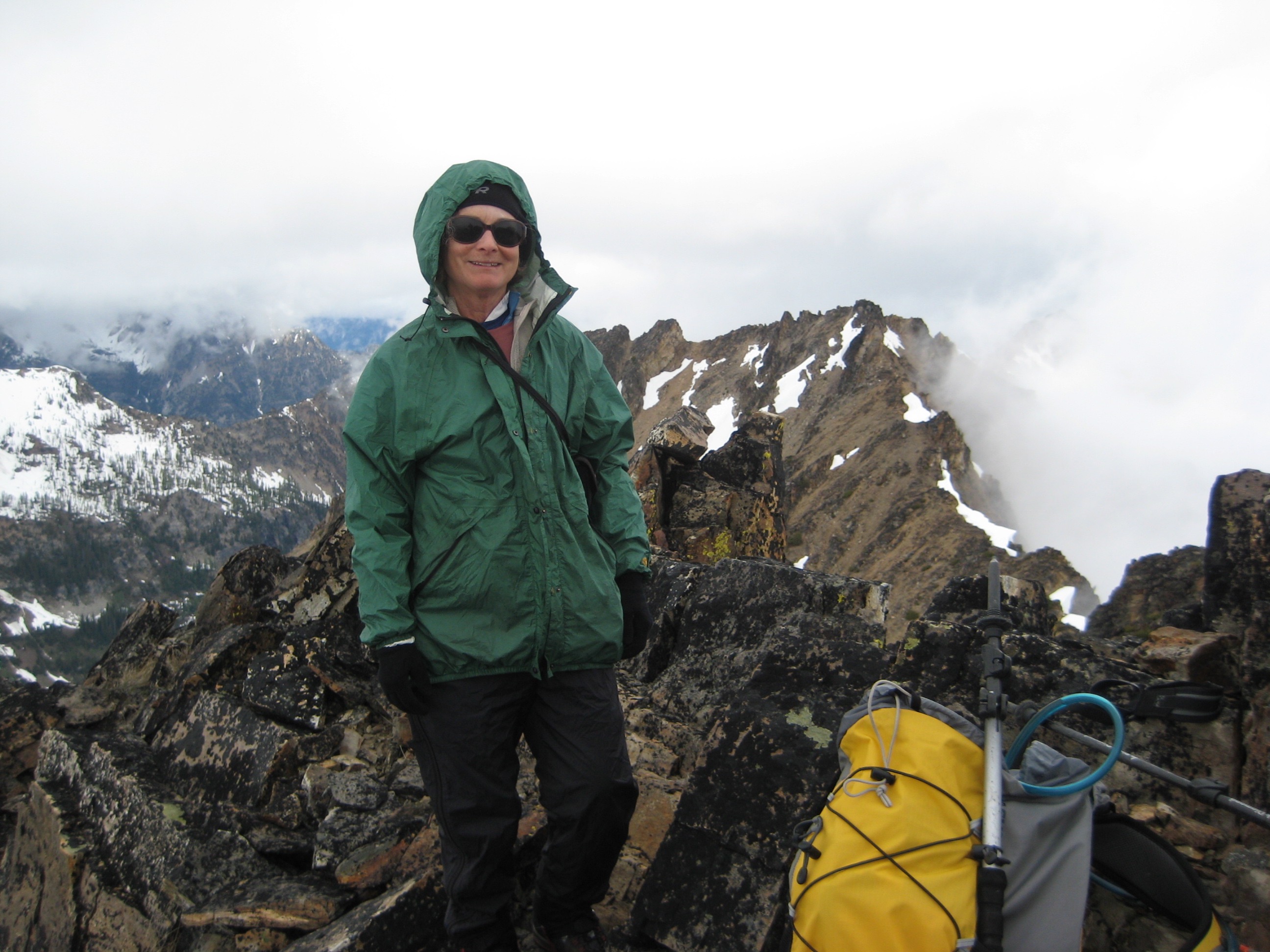 mountain climber on the summit of rocky Flora Mountain in the Stehekin Mountains with a cloud covered ridge line in the background