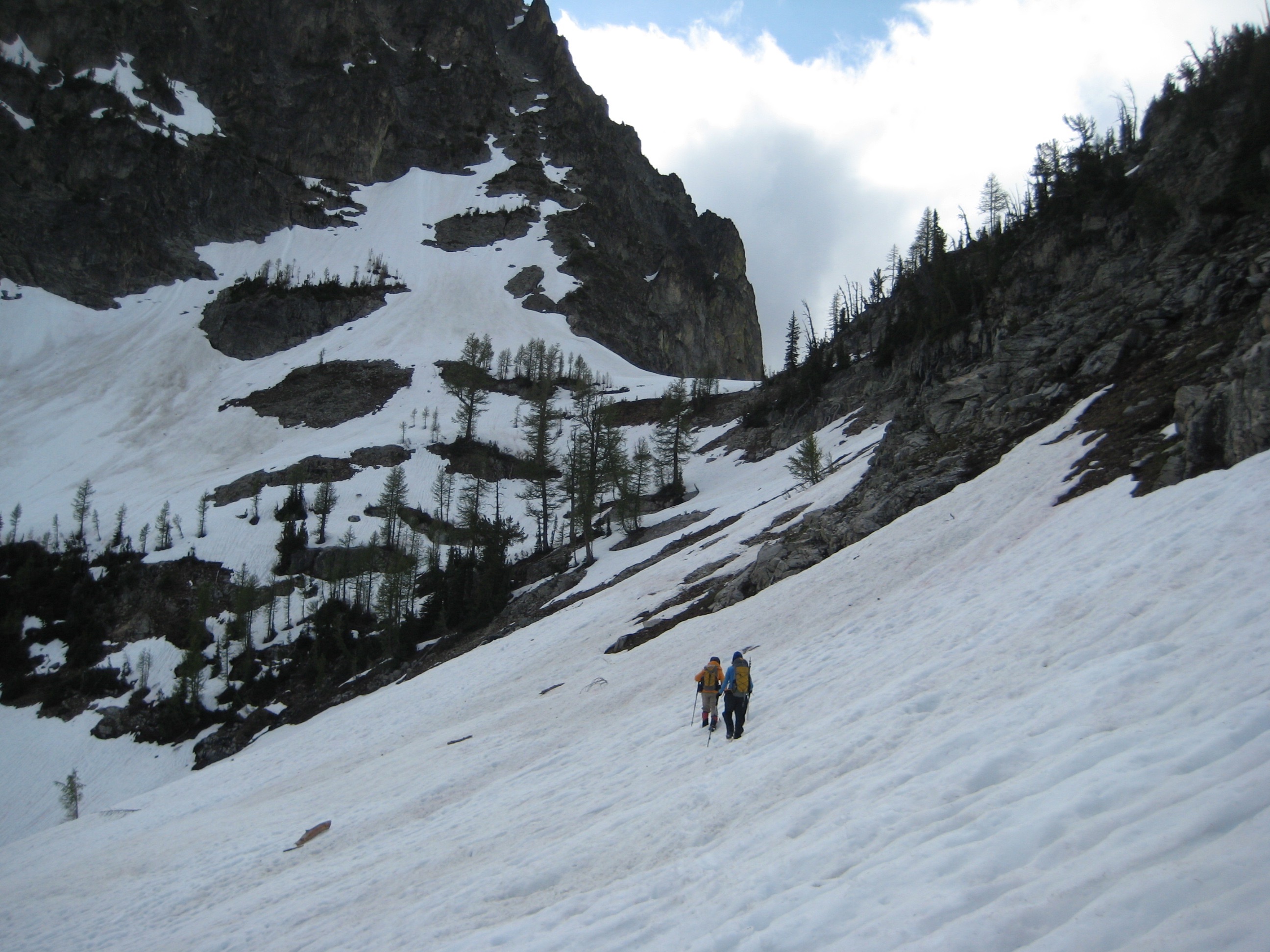 mountain climbers traversing snow field late in the day heading for the low spot on the ridge in the Stehekin Mountains