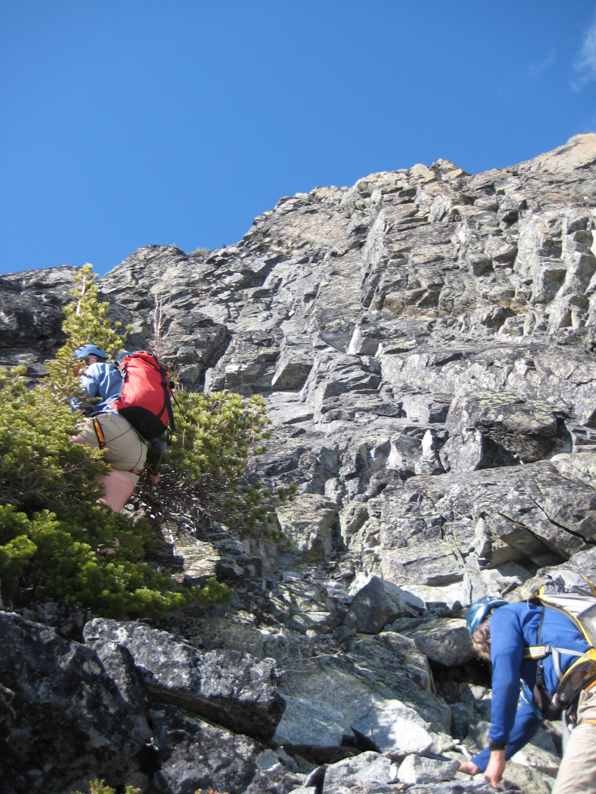 mountain climbers scrambling through brush with the steep rocky face of Black Tower in the Stehekin Mountains