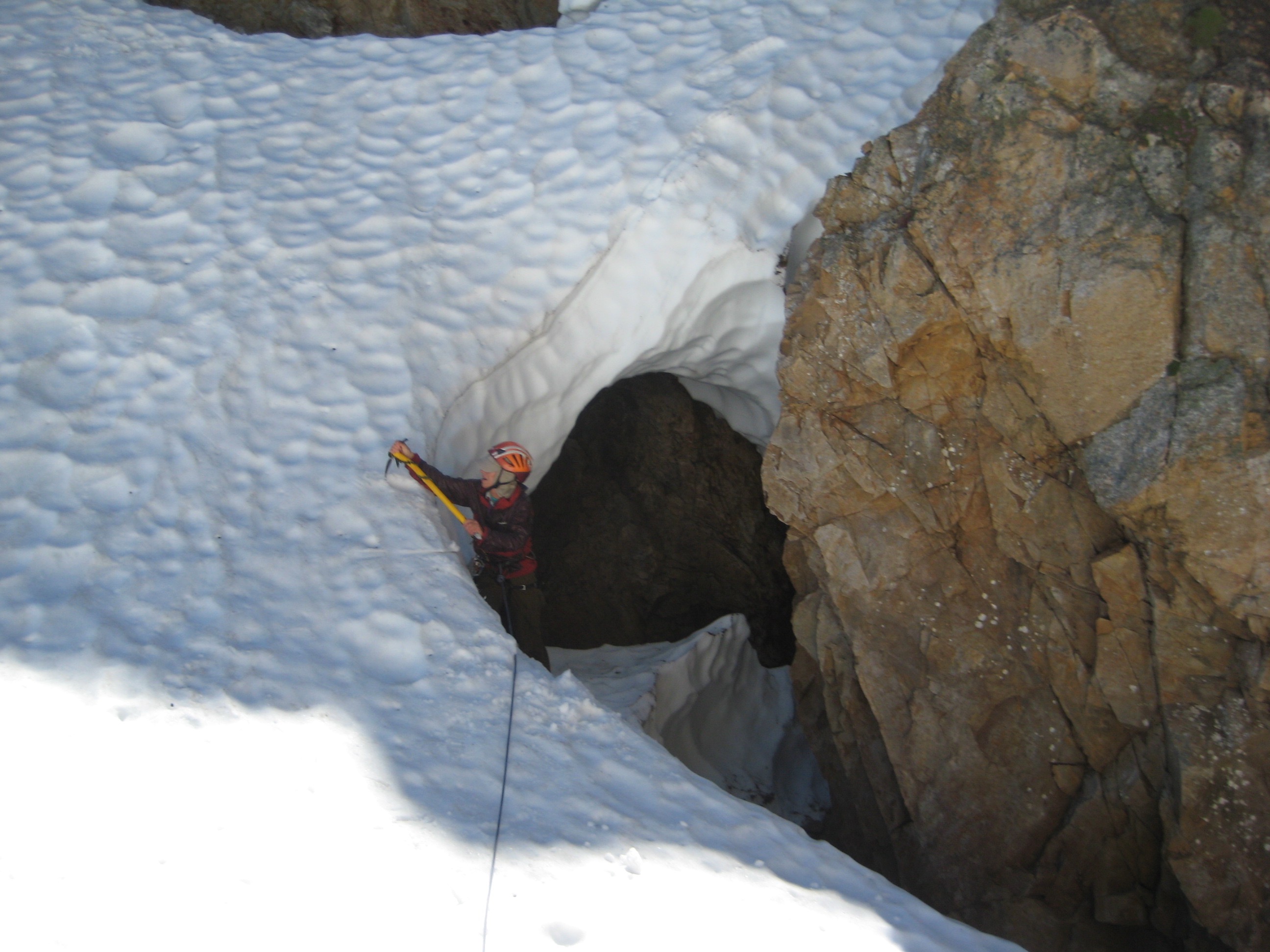 mountain climber using ice axe to climb out of a snow cave leading to the rock on Mt Terror
