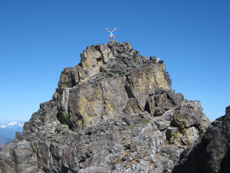 A mountain climber waves from the rocky summit of Mt Ballard