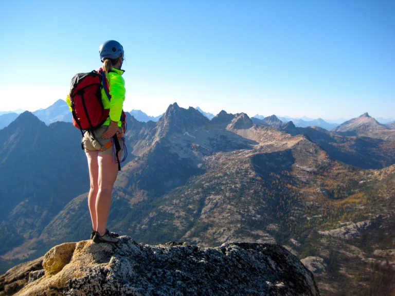 A rock climber stands atop Liberty Bell Mountain overlooking a craggy range of peaks