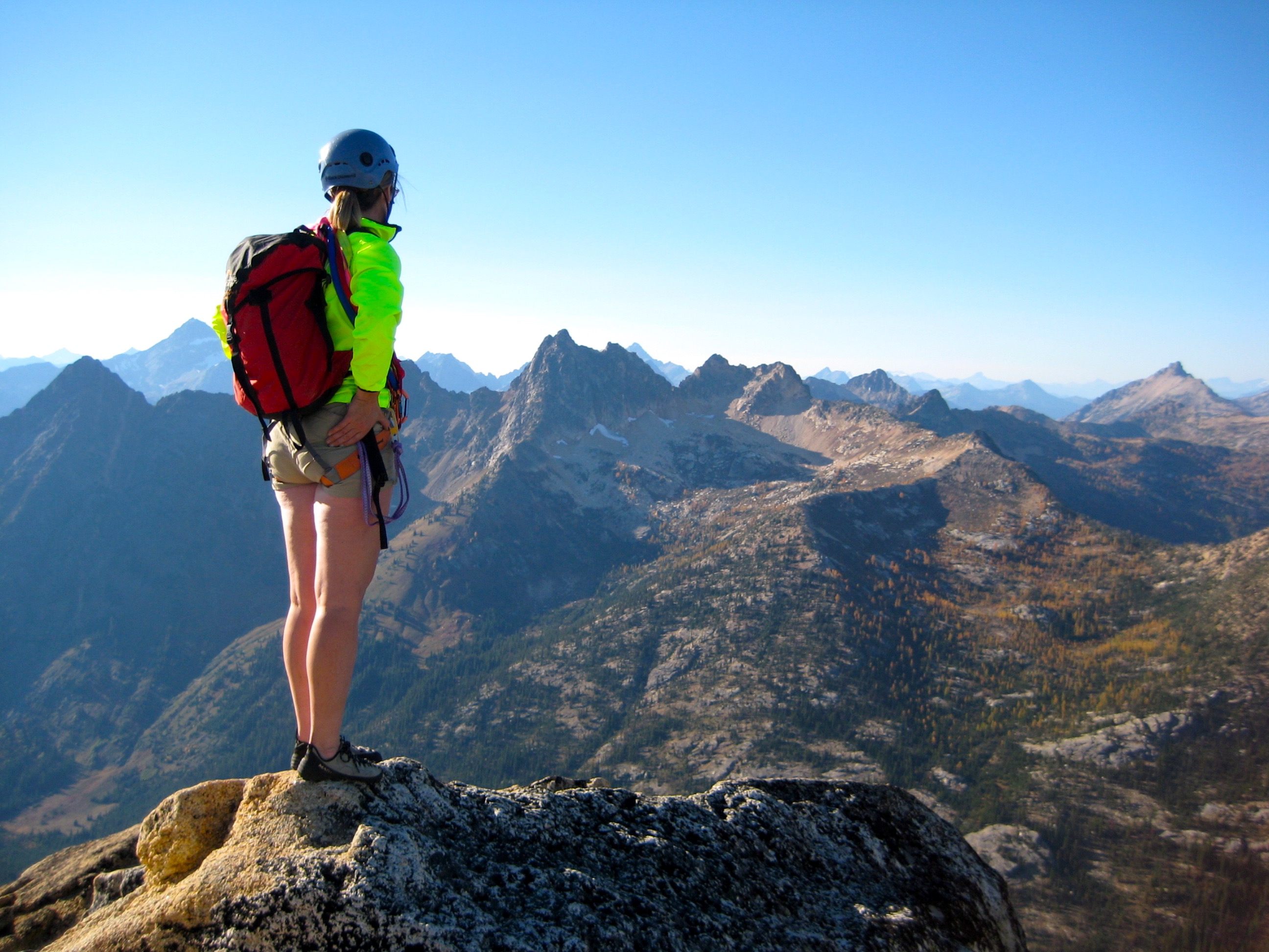 A rock climber stands atop Liberty Bell Mountain overlooking a craggy range of peaks