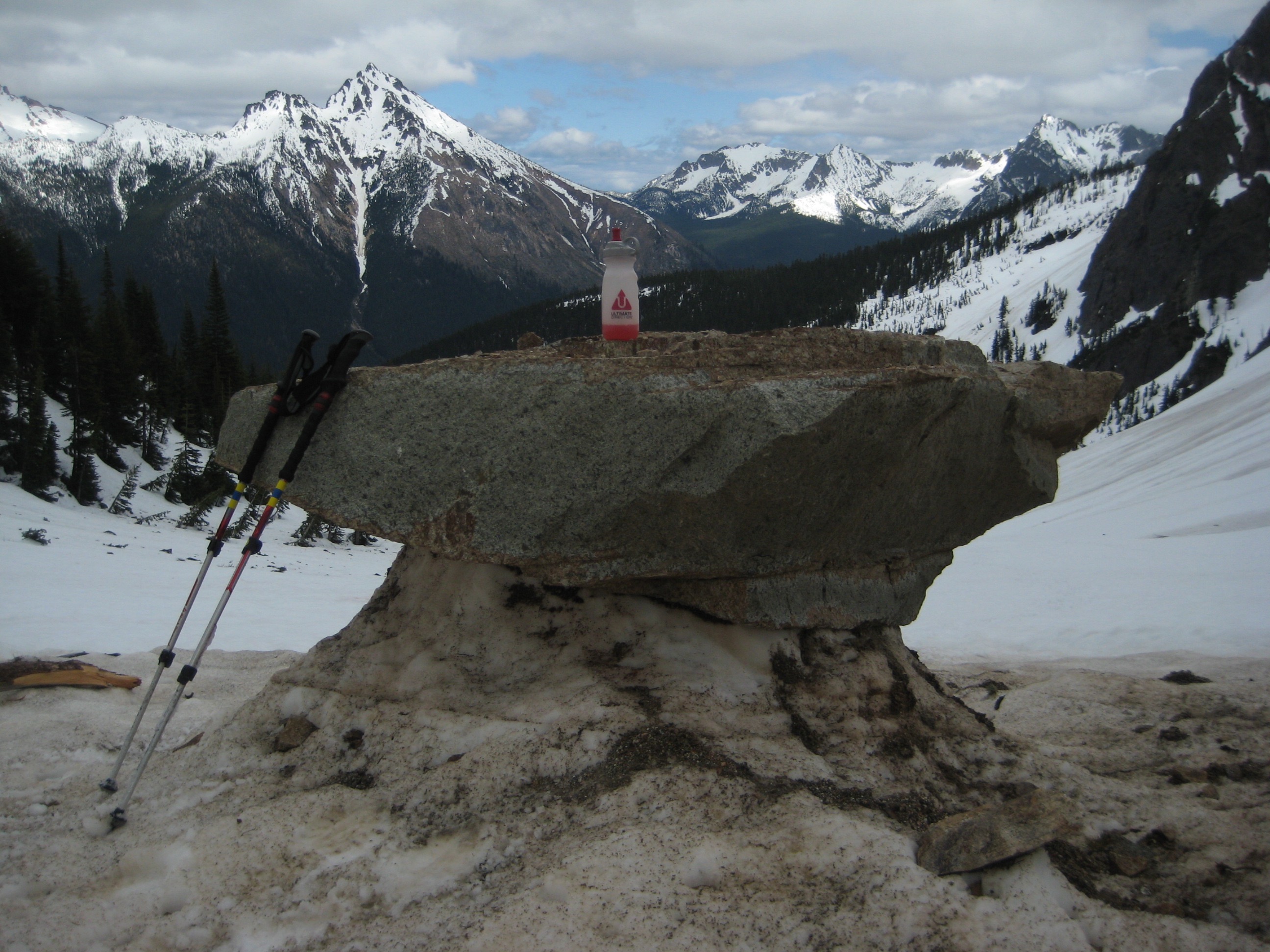 rock table with mountain climbers water bottle and hiking poles under Easy Pass in the North Cascades with snow capped mountains in the background