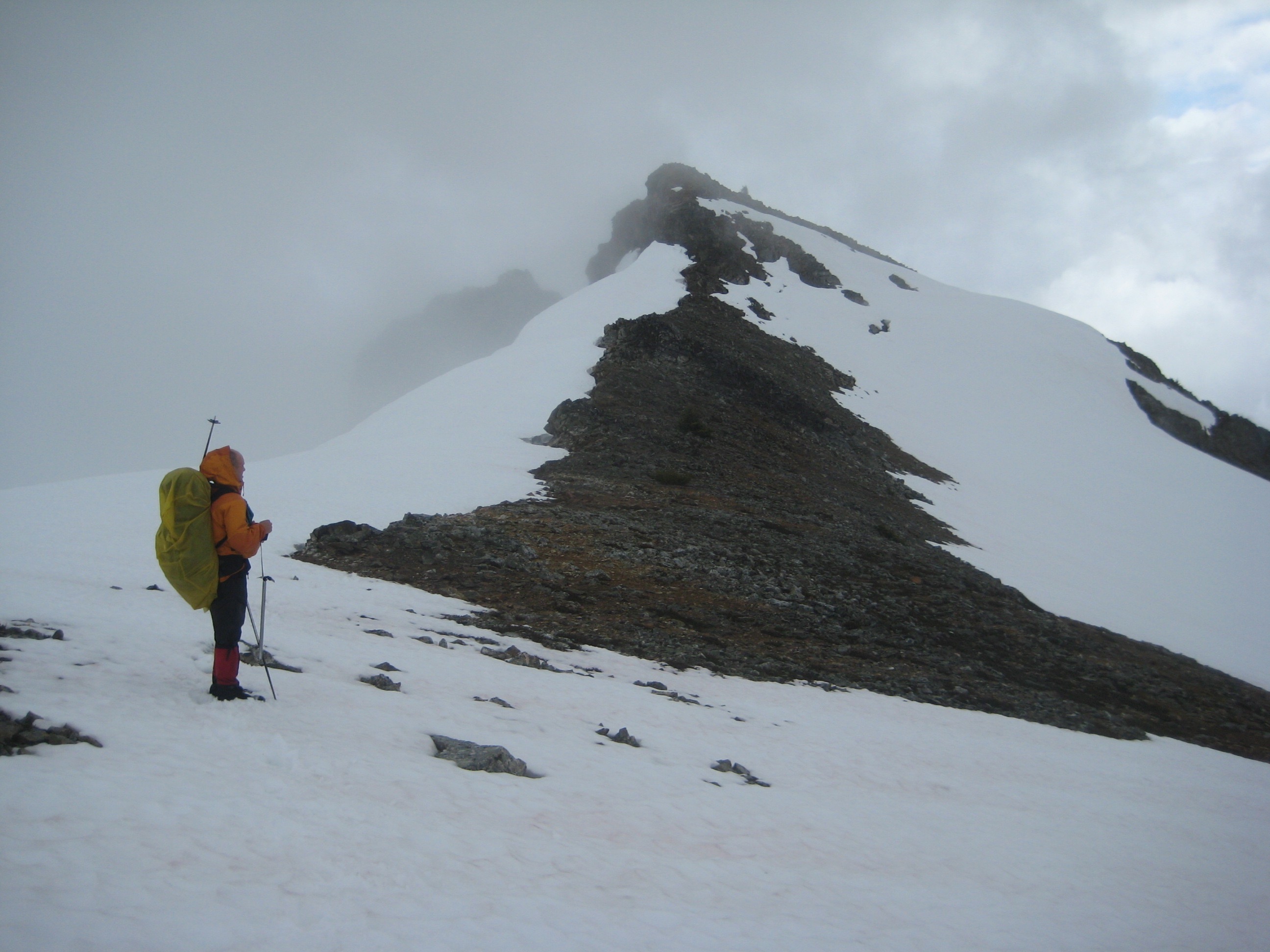 mountain climber assessing the snow and dirt covered south ridge of Mt Prophet in North Cascades National Park