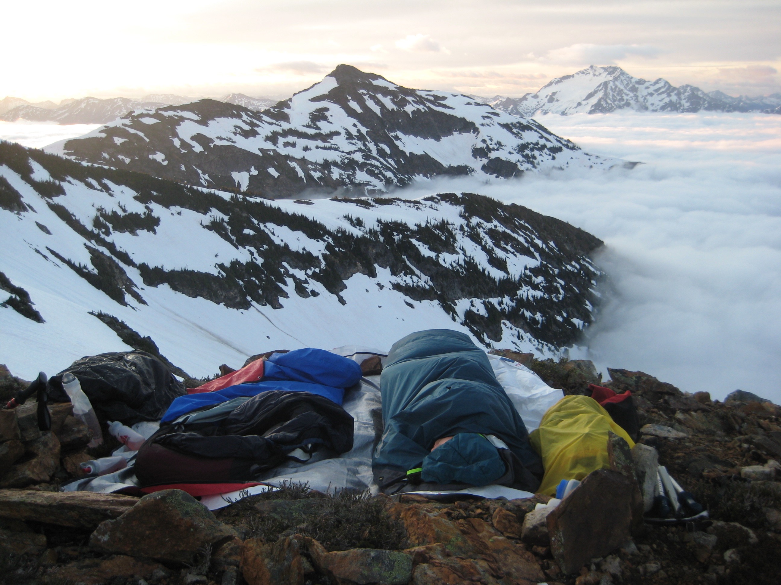 mountain climbers bivey camp on the shoulder of Mt Prophet with the mountains of North Cascades National Park in the distancce above valley fog