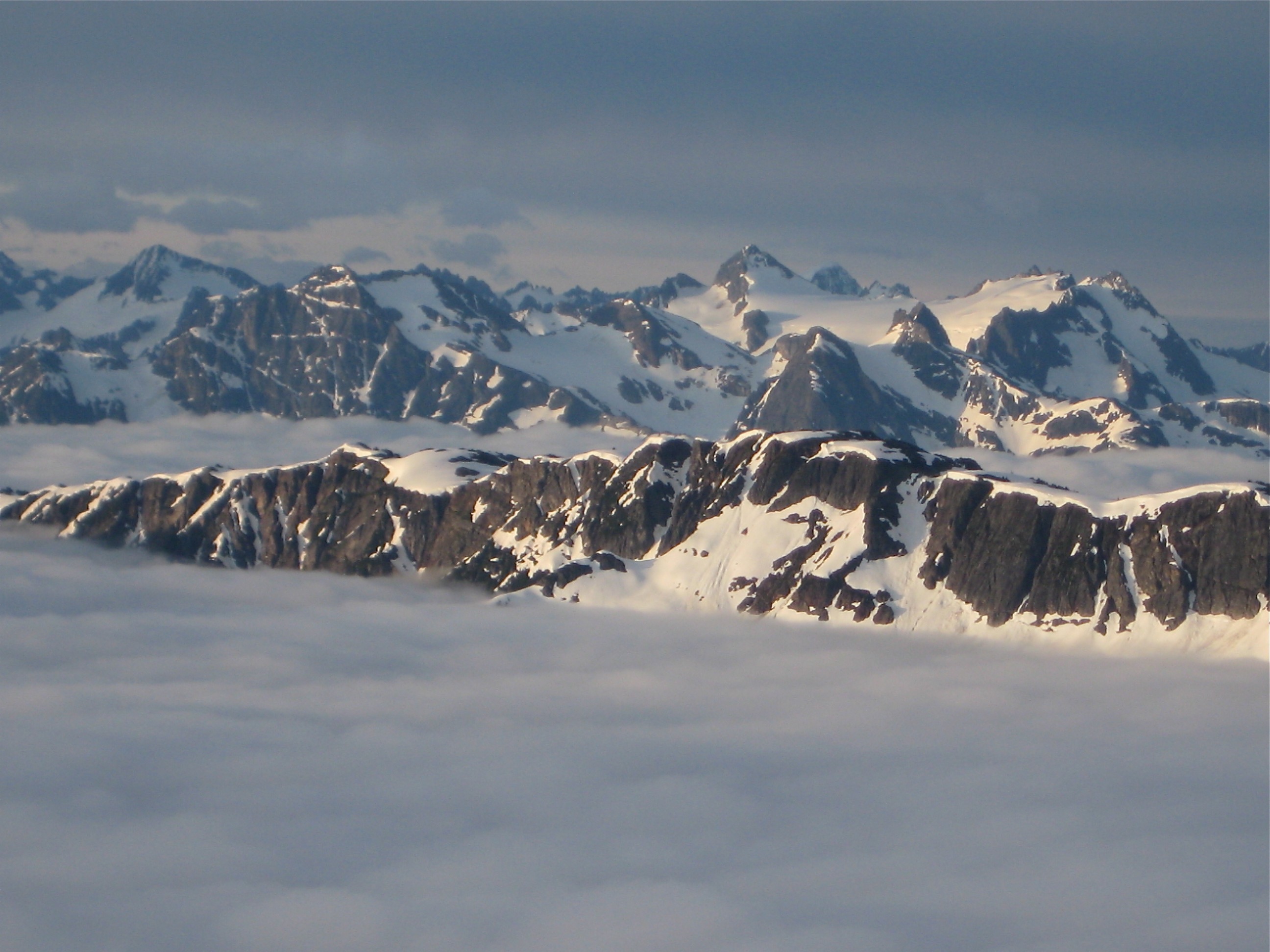 Snowfield Peak and Colonical Peak rise above valley fog in the distance as seen from climbers camp on the shoulder of Mt Prophet in North Cascades National Park