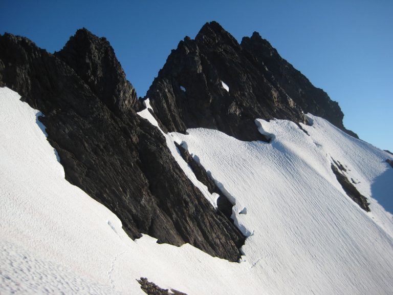 Steep snow slopes lead up the rocky North Face of West Anderson Peak in the Olympic Mountains