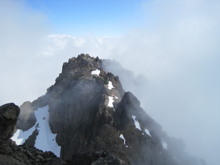 The rocky summit horn of North Brother peak reveals itself in a fog bank in the Olympic Mountains