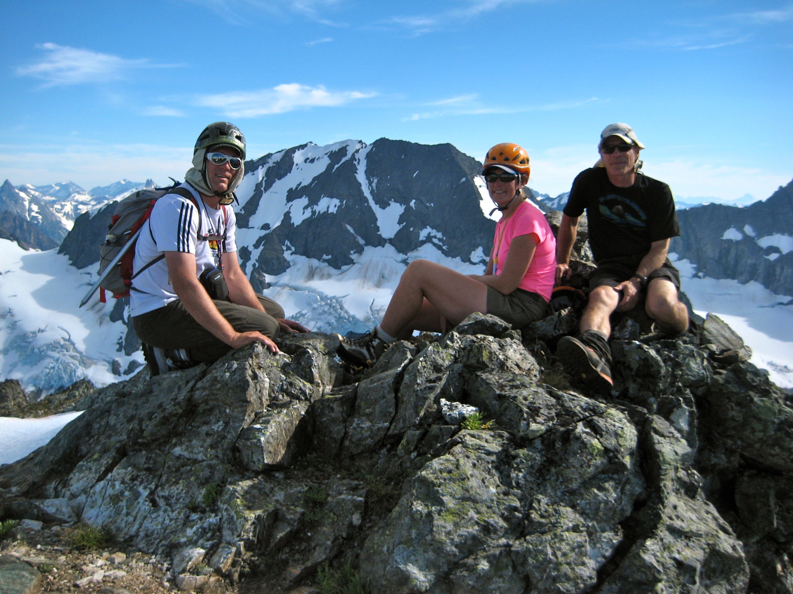 mountain climbers sit on the rocky summit of Hurry-Up Peak with mountains in the Glacier Peak Wilderness