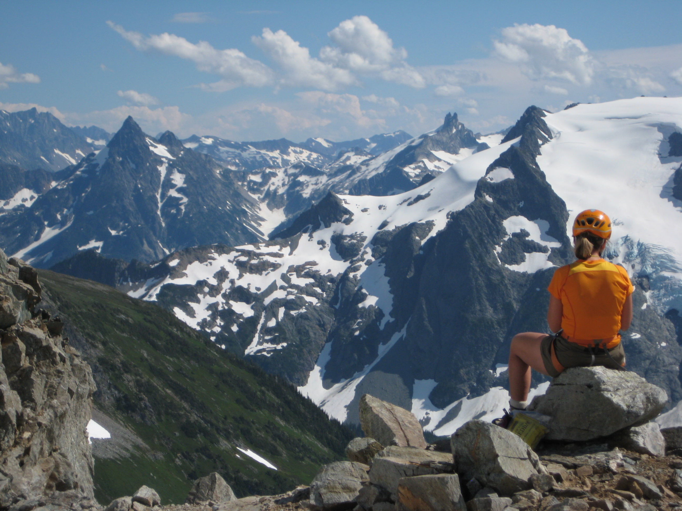 mountain climber taking a break in the rocks on the Ptarmigan Traverse with Agnes Mountain and Gunsight Peak in the background